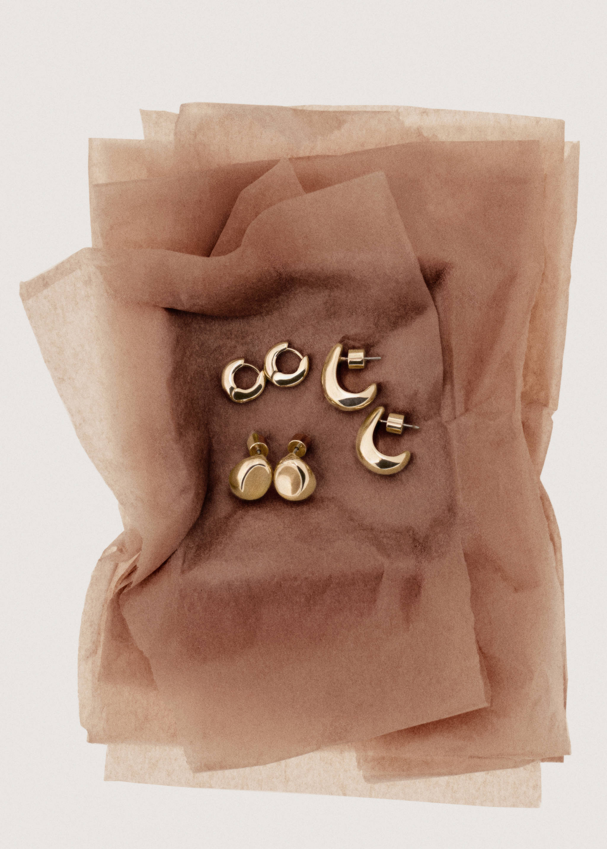 Three pairs of gold-finish metal earrings arranged on brown tissue paper.