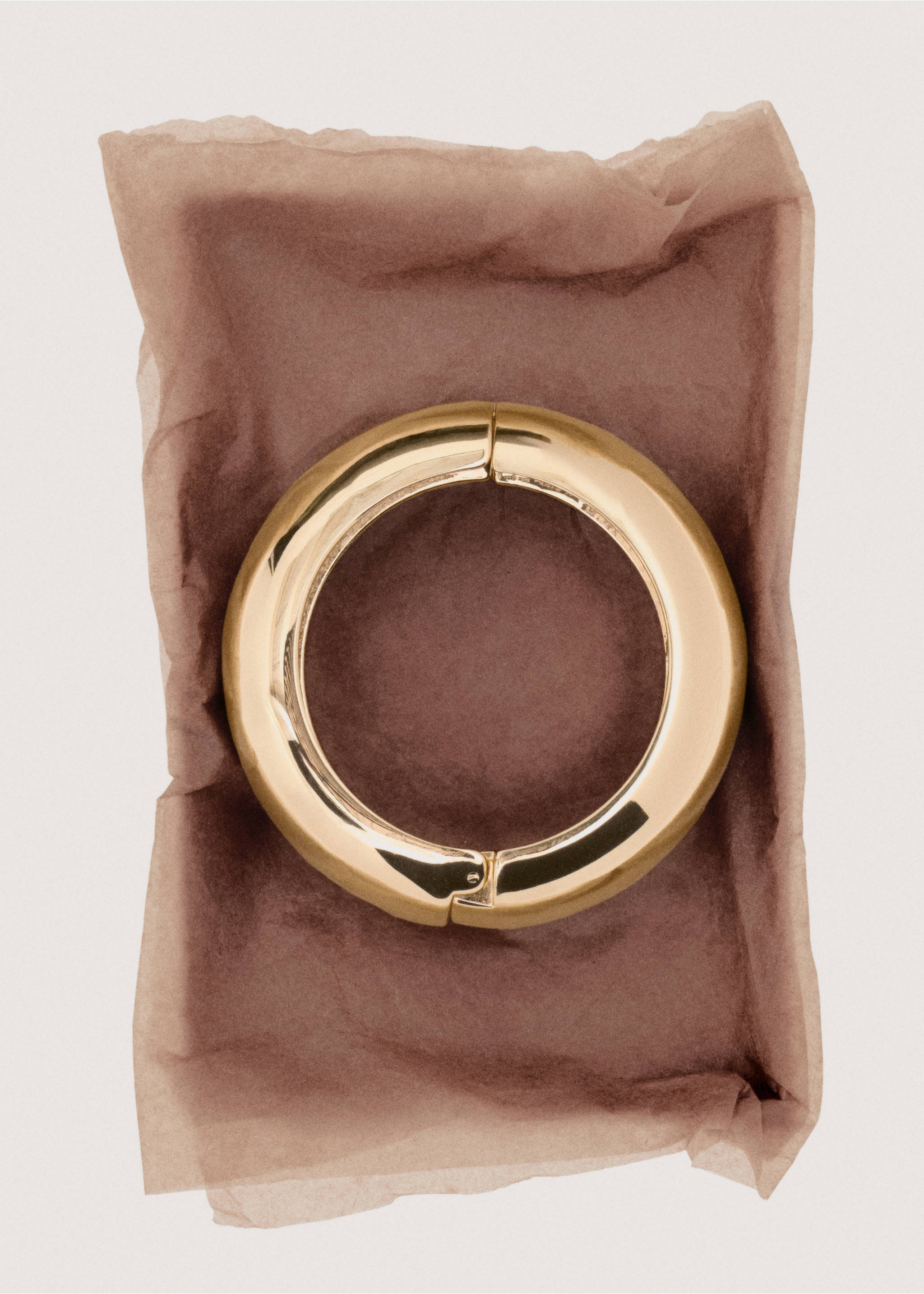 Thick, polished gold-tone rigid bangle bracelet resting on tissue paper., Gold. Ref: 27091284-00.