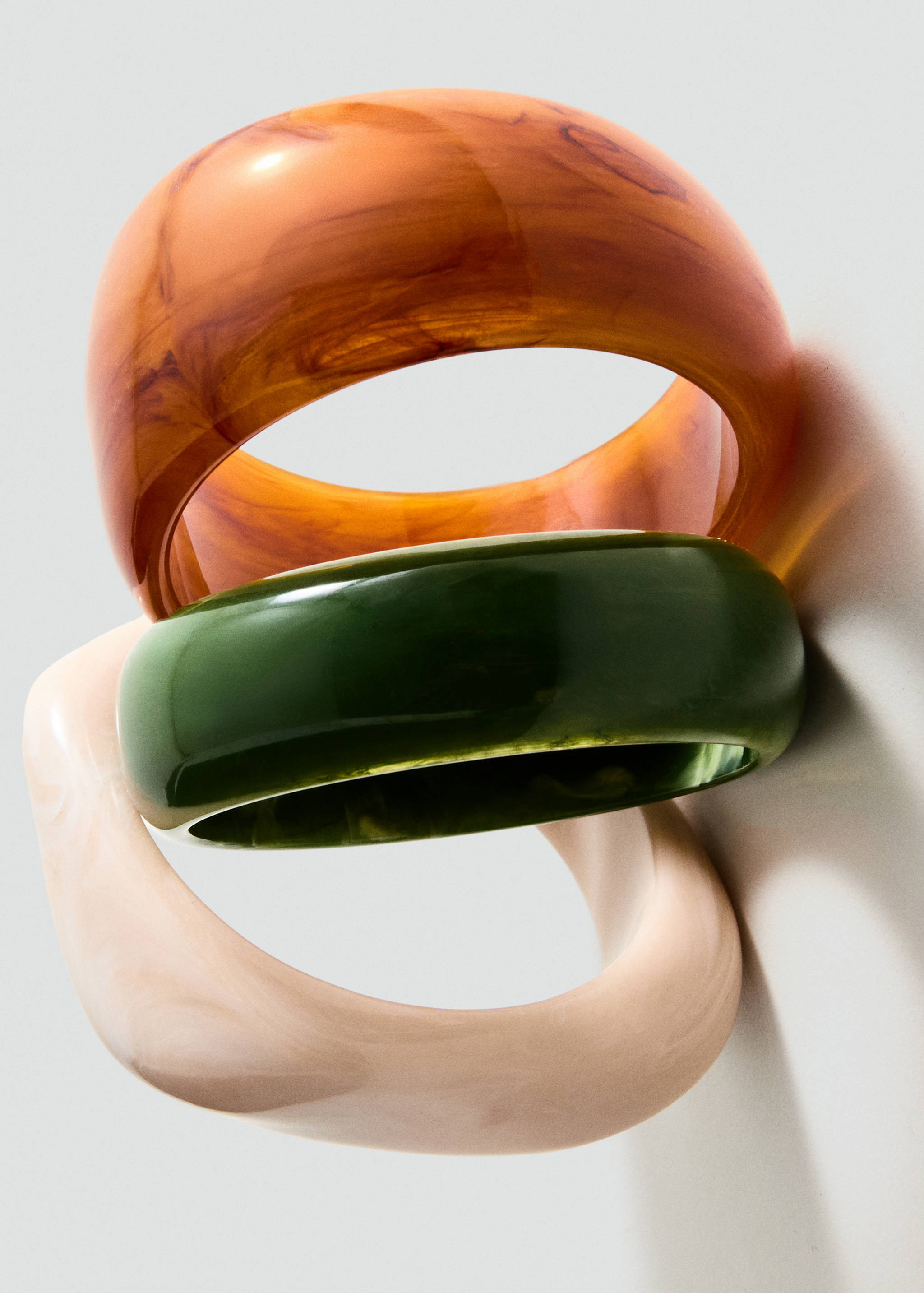 Close-up of three chunky resin bangles in amber, dark green, and beige.