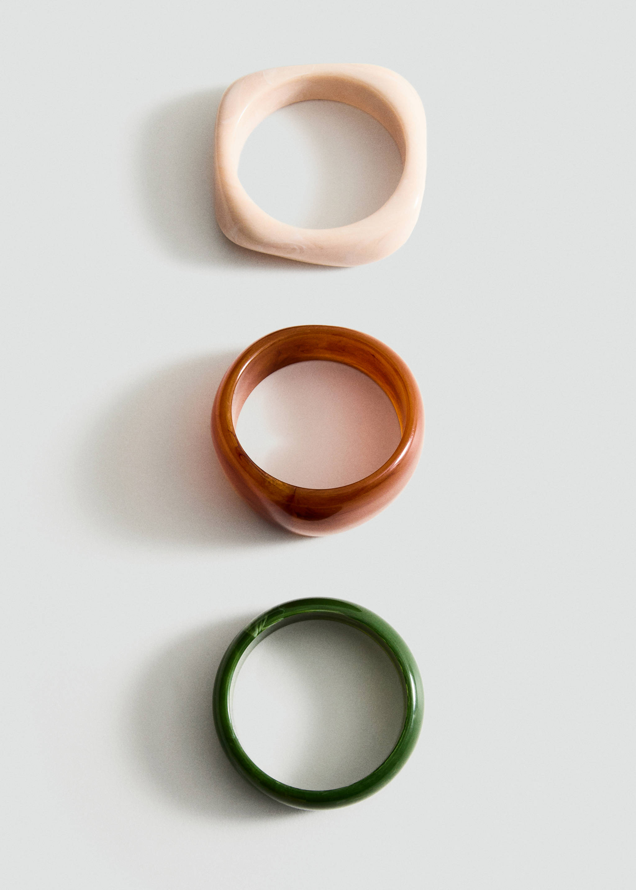 Three rigid bangles in pale pink, amber brown, and dark green.