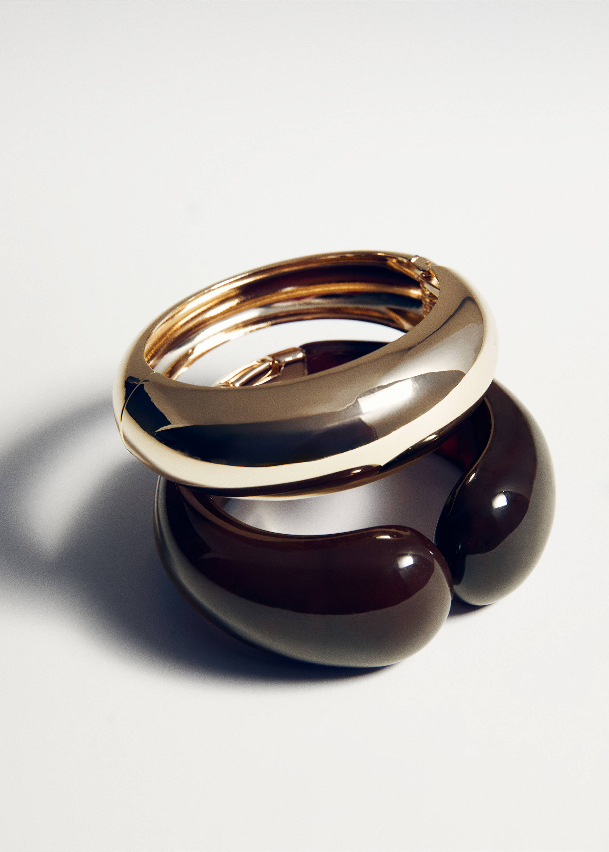 A shiny gold-toned metallic bangle stacked over a thick, glossy dark brown resin cuff., Gold. Ref: 27092922-00.