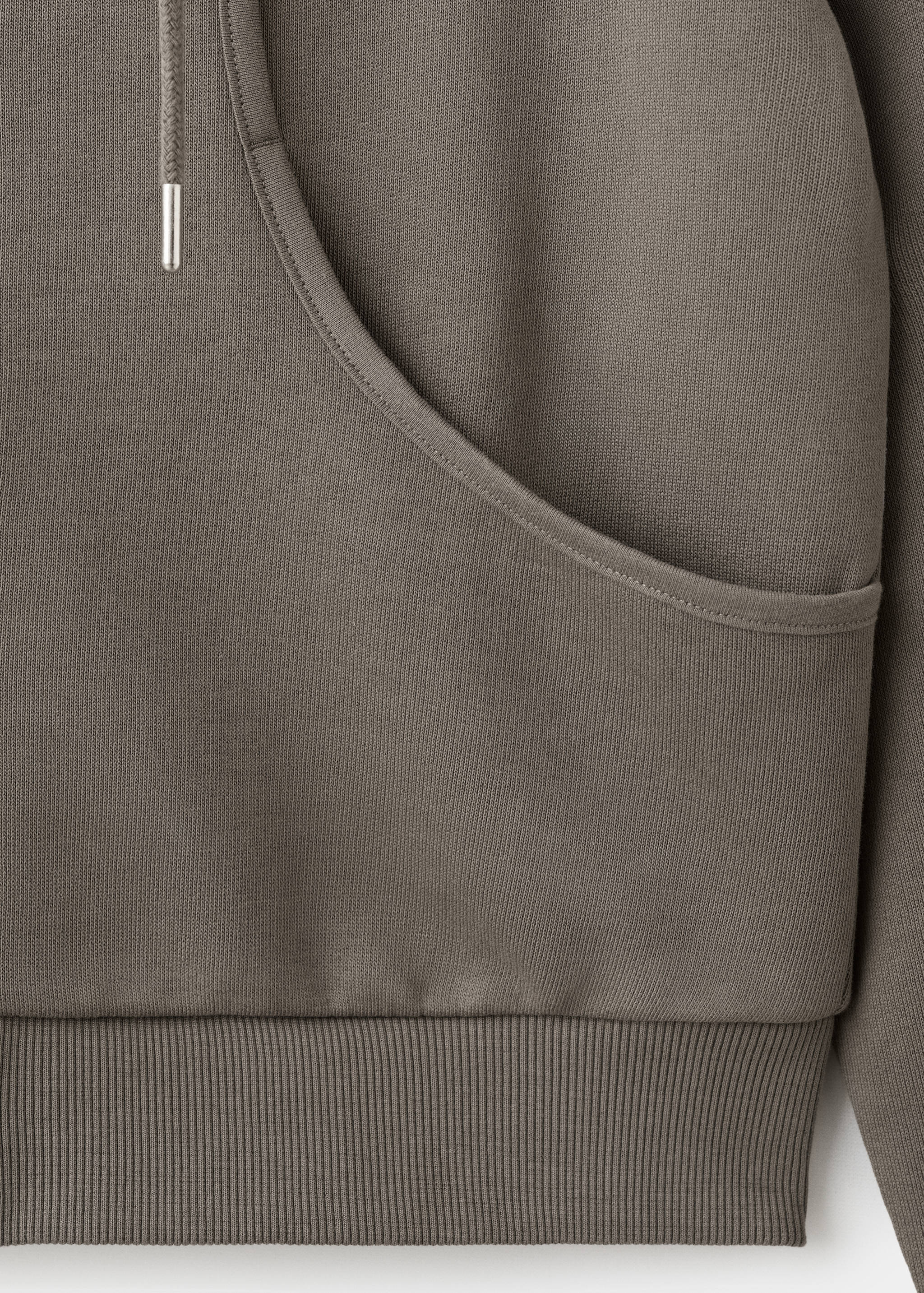 Close-up of fabric and kangaroo pocket detail on a greyish-brown hoodie.