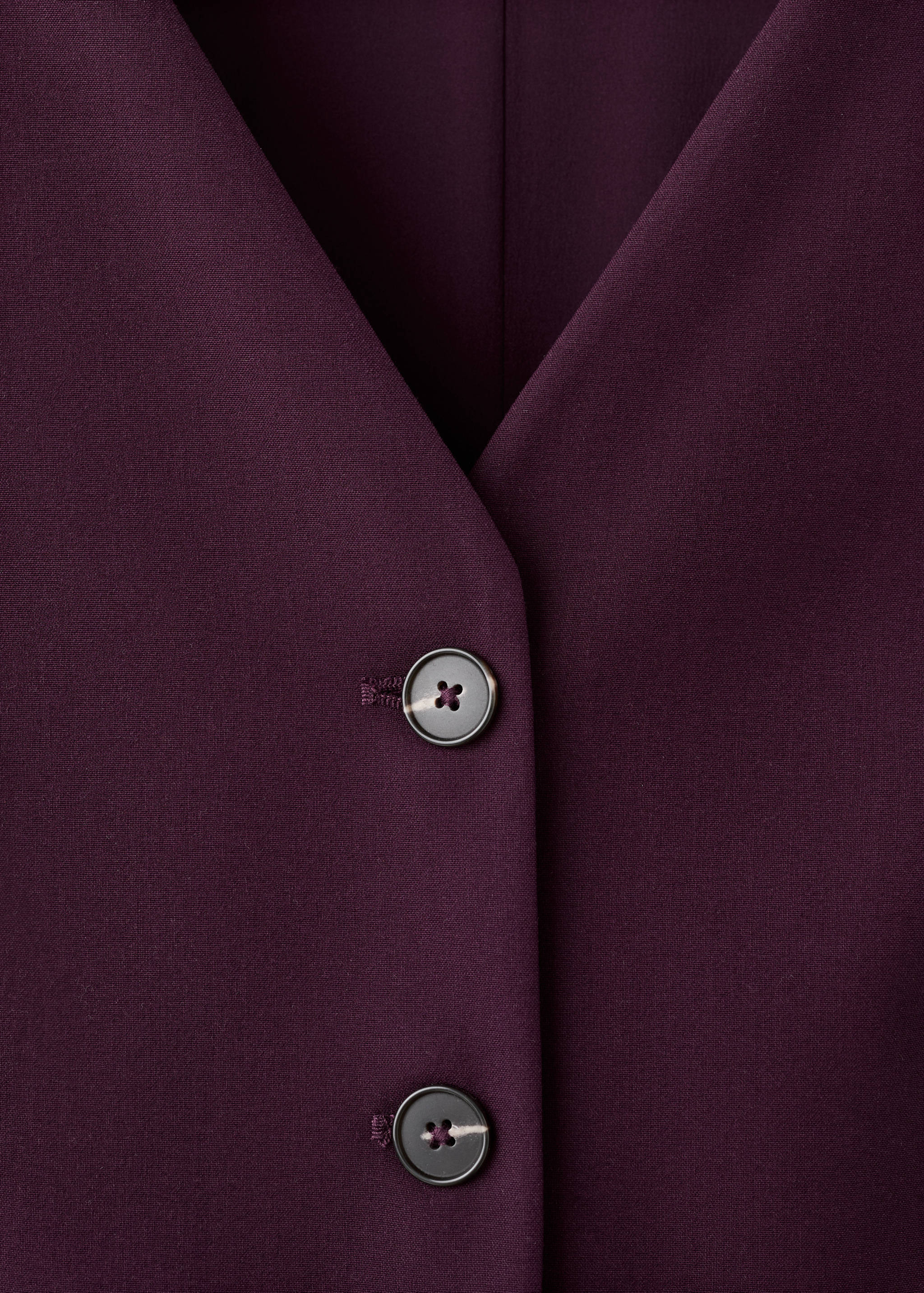Close-up of a dark purple jumpsuit V-neck and button detail.