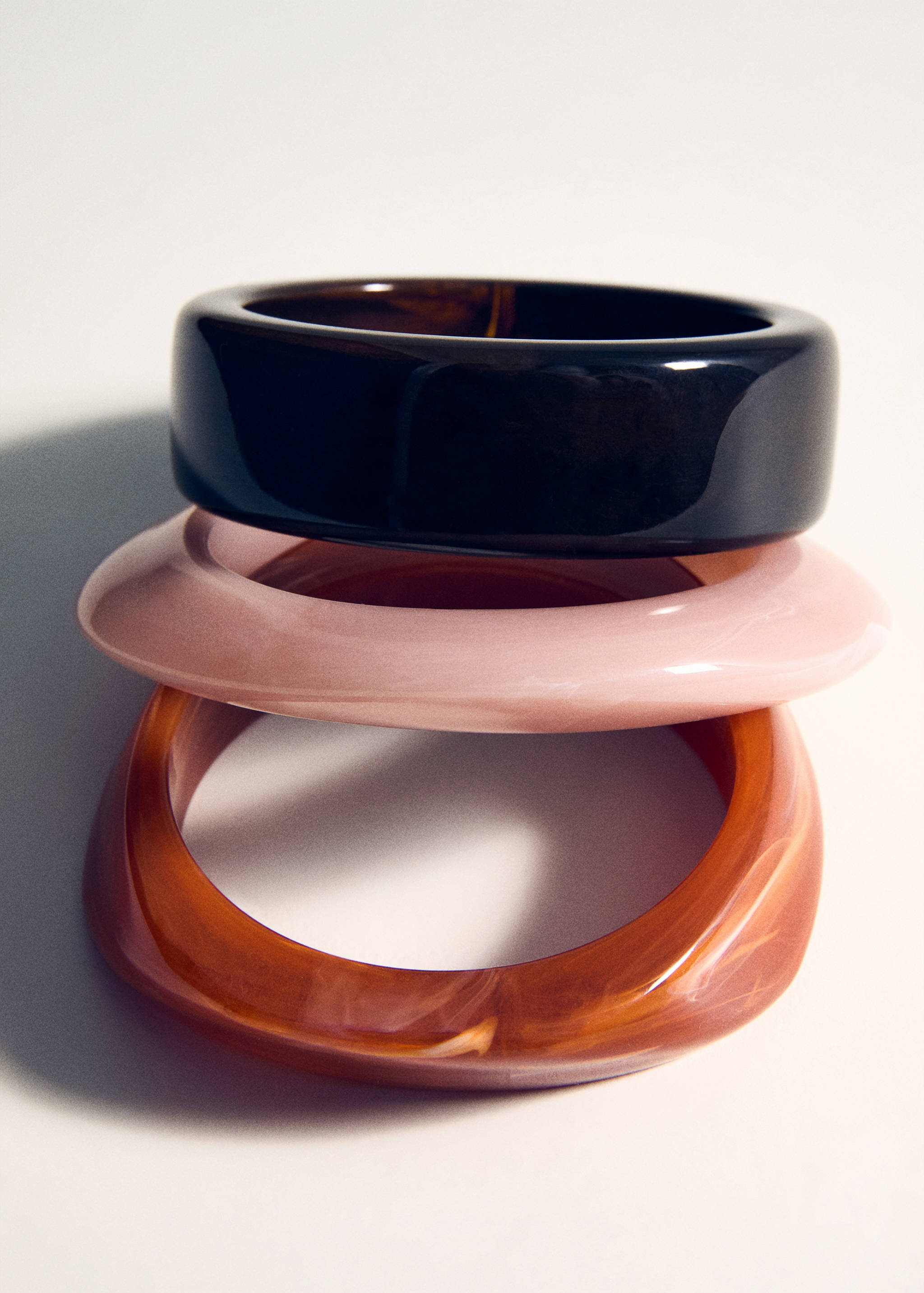 Three stacked chunky resin bangles in black, light pink, and marbled amber.