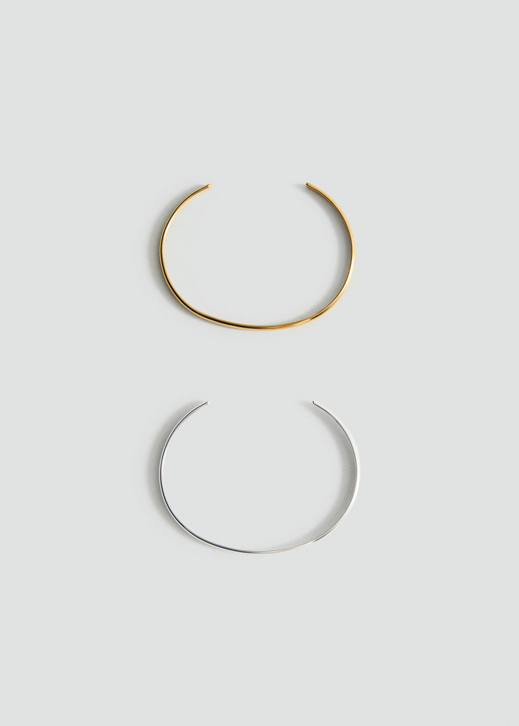 Gold and silver metal open cuff bracelets in a still life.