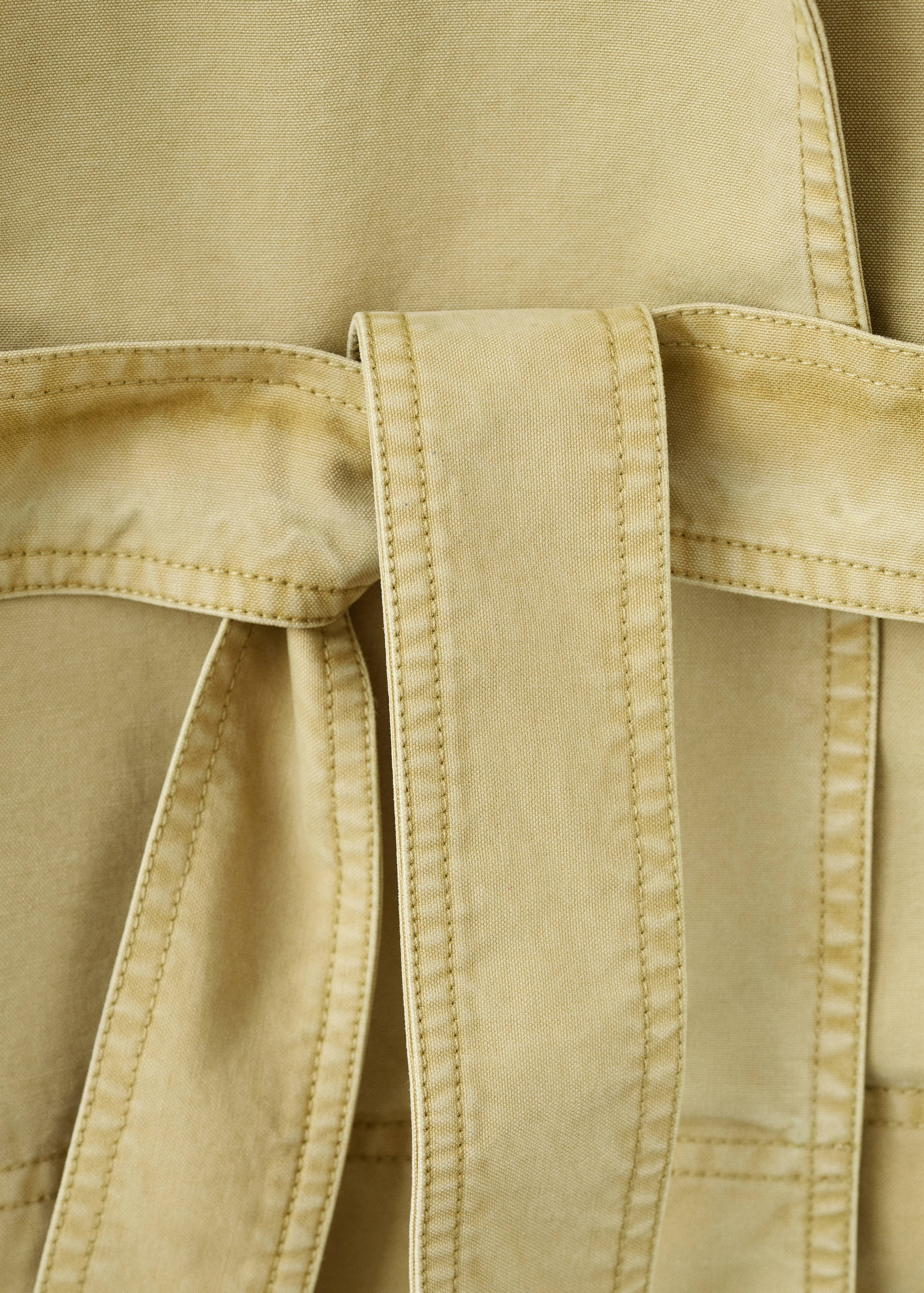 Primer plano del detalle del cinturones de tela en una parka beige.