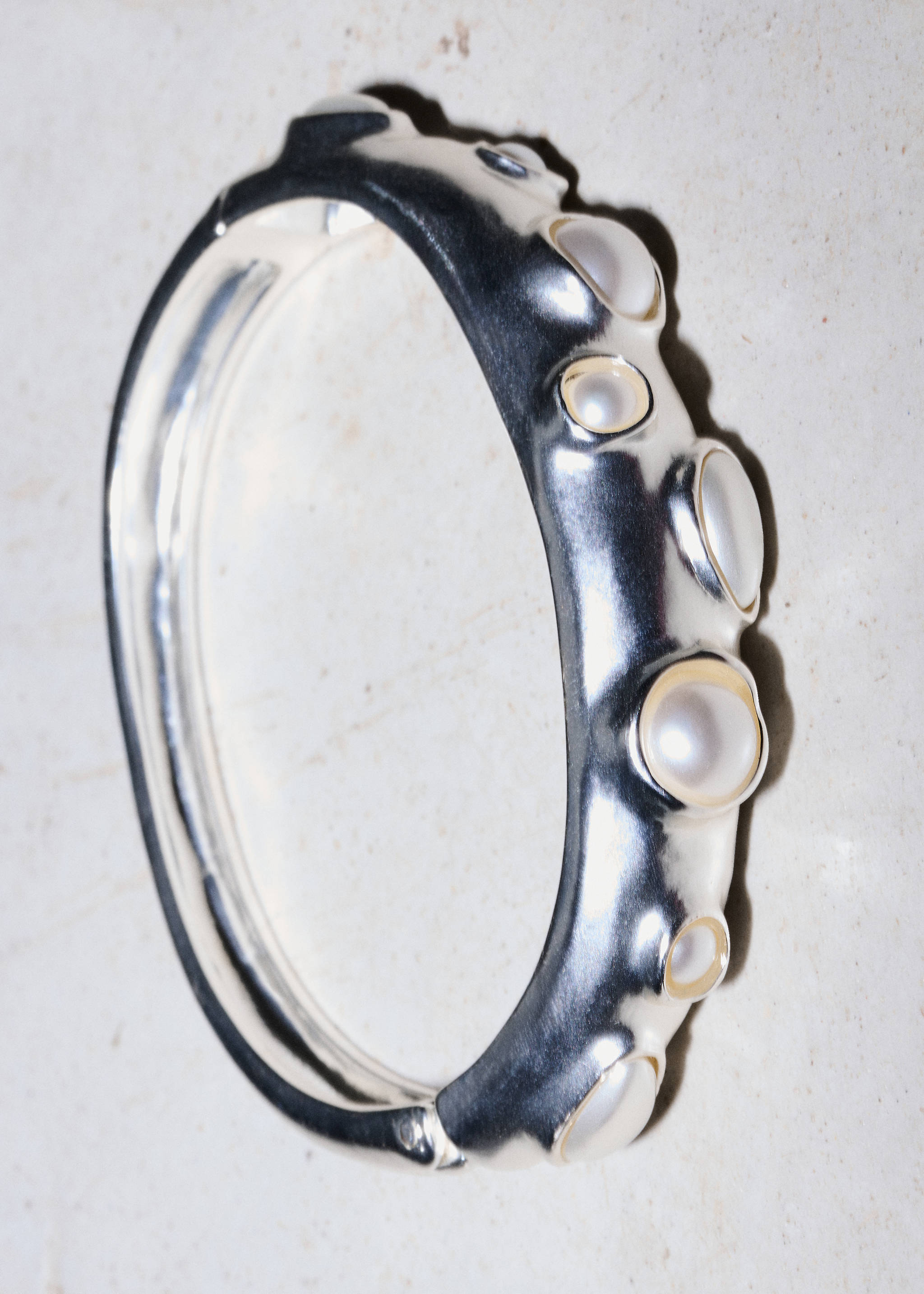 Chunky silver-finished rigid bangle bracelet embellished with embedded white pearls.