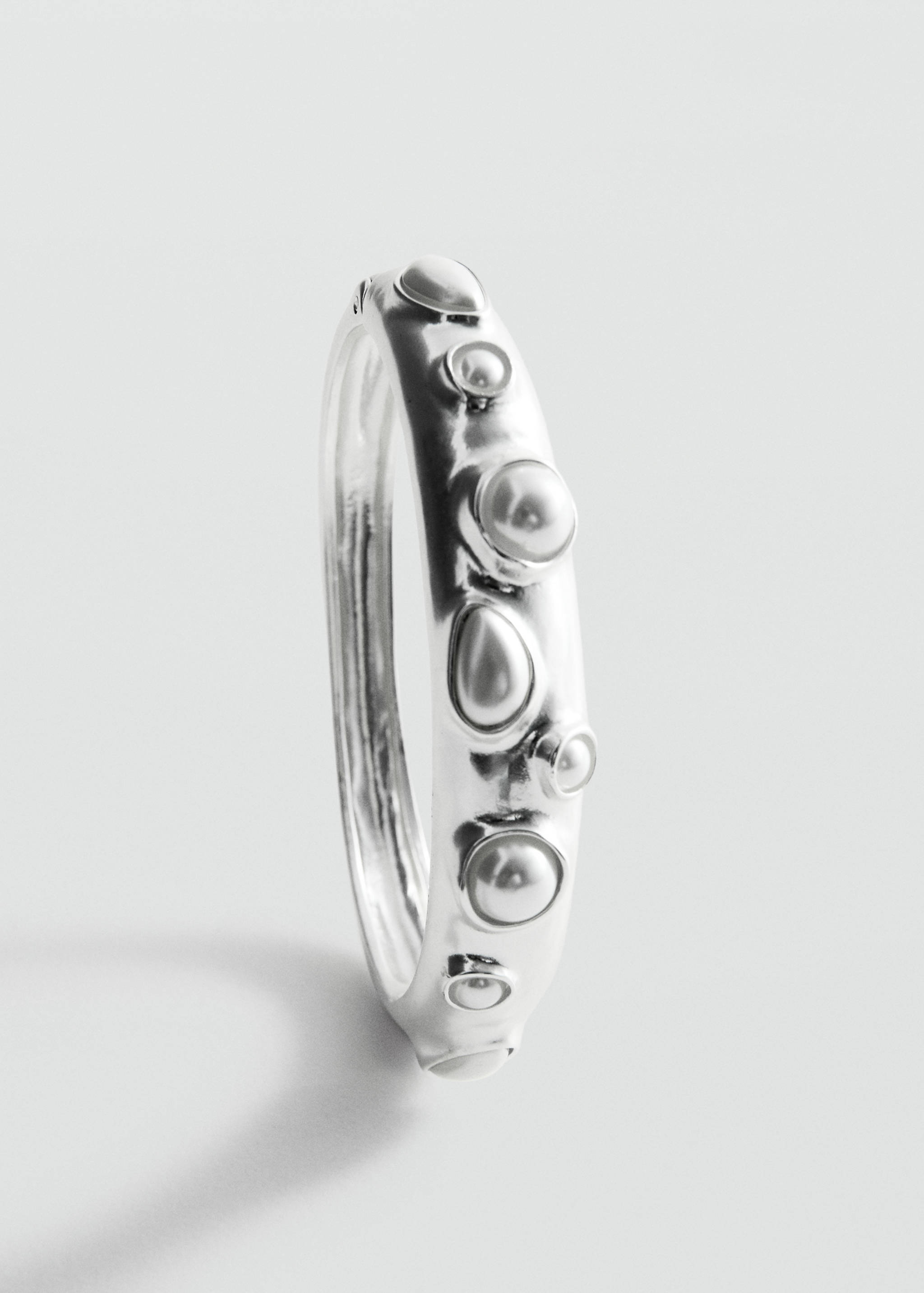 Close-up of a silver-coloured rigid bracelet with embedded pearl-like beads.
