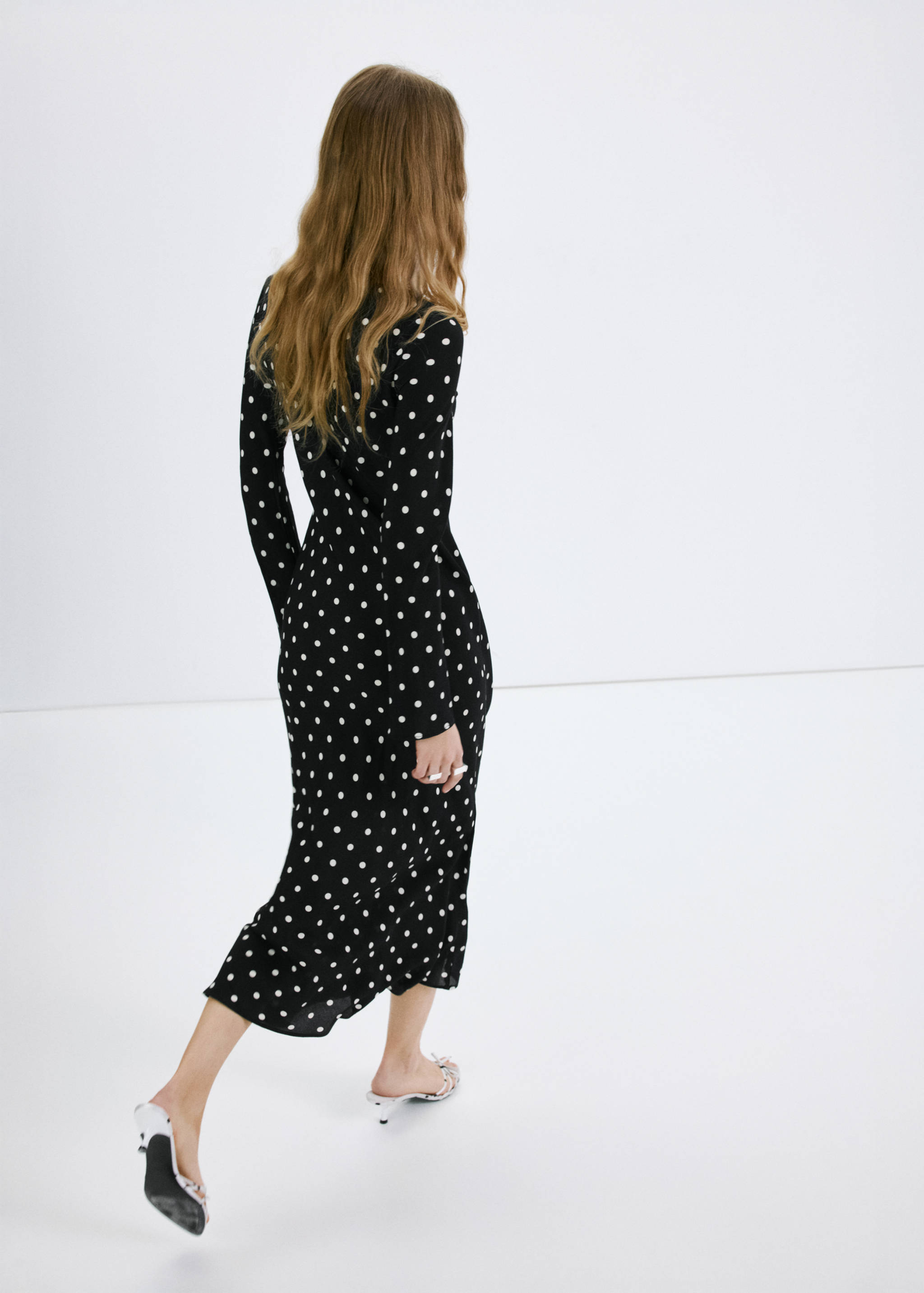 Back view of a black polka-dot midi dress with long sleeves.