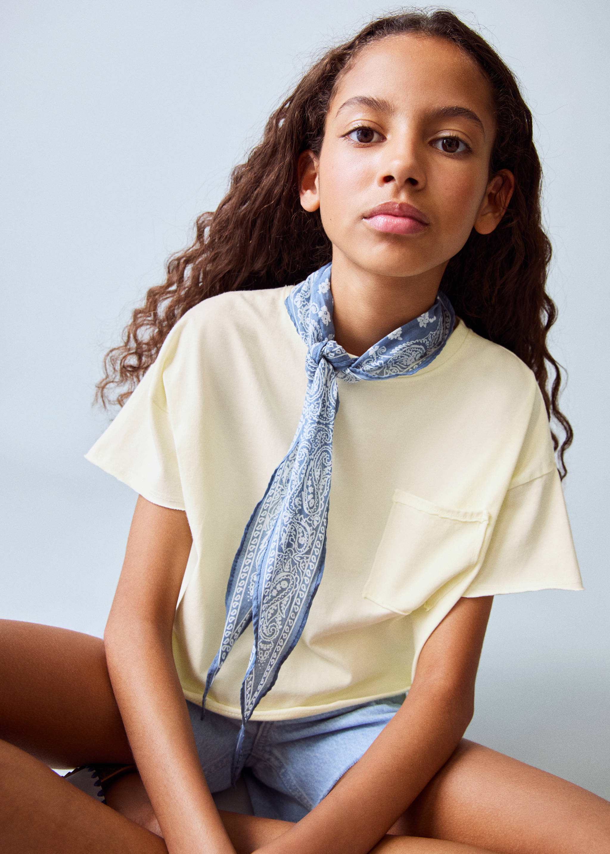 Pale yellow short-sleeved t-shirt with a chest pocket, worn with a paisley scarf.