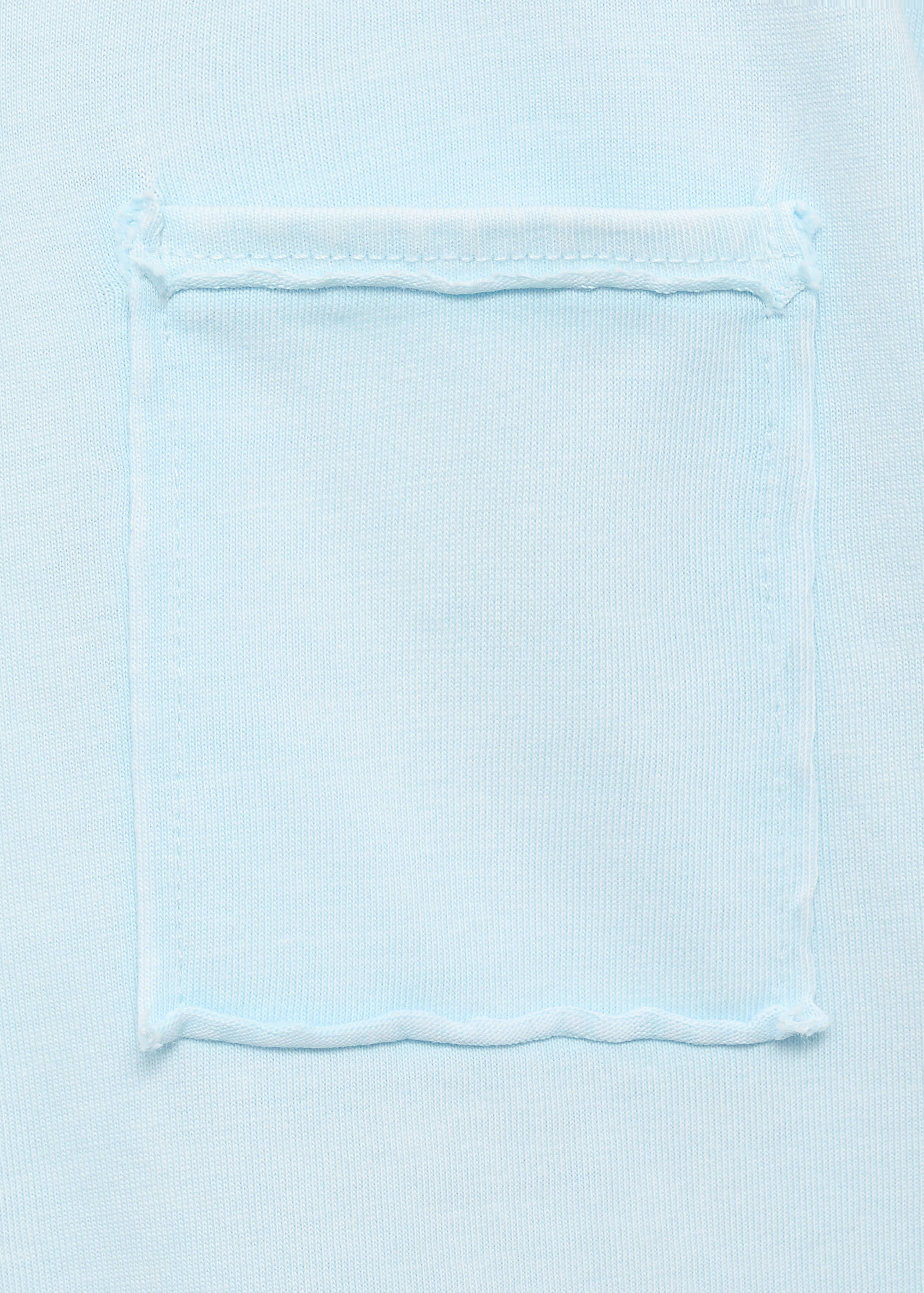 Close-up of a light blue t-shirt pocket with raw edges.
