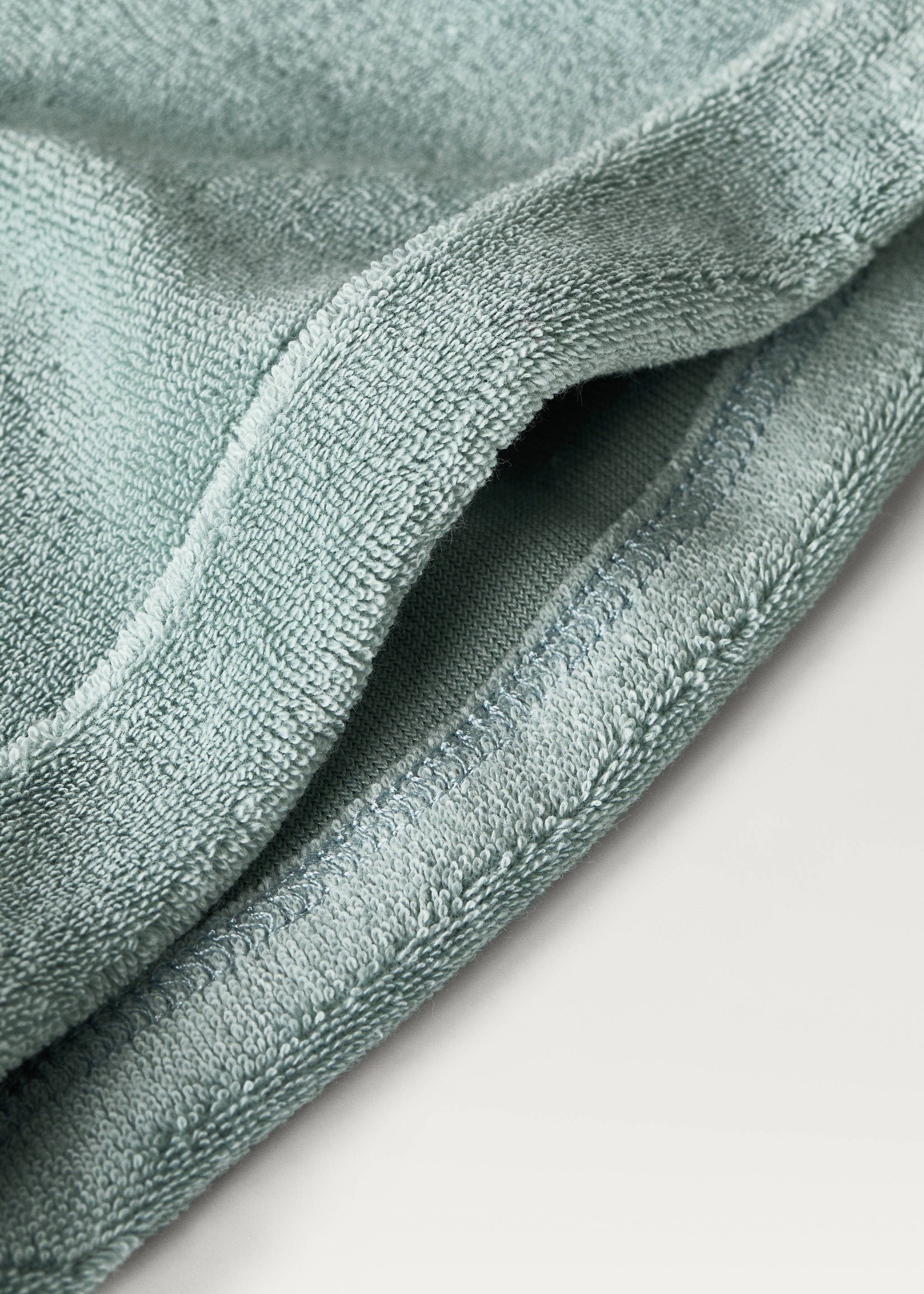 Sage green terry cotton product detail with textured loop pile and stitched edge.