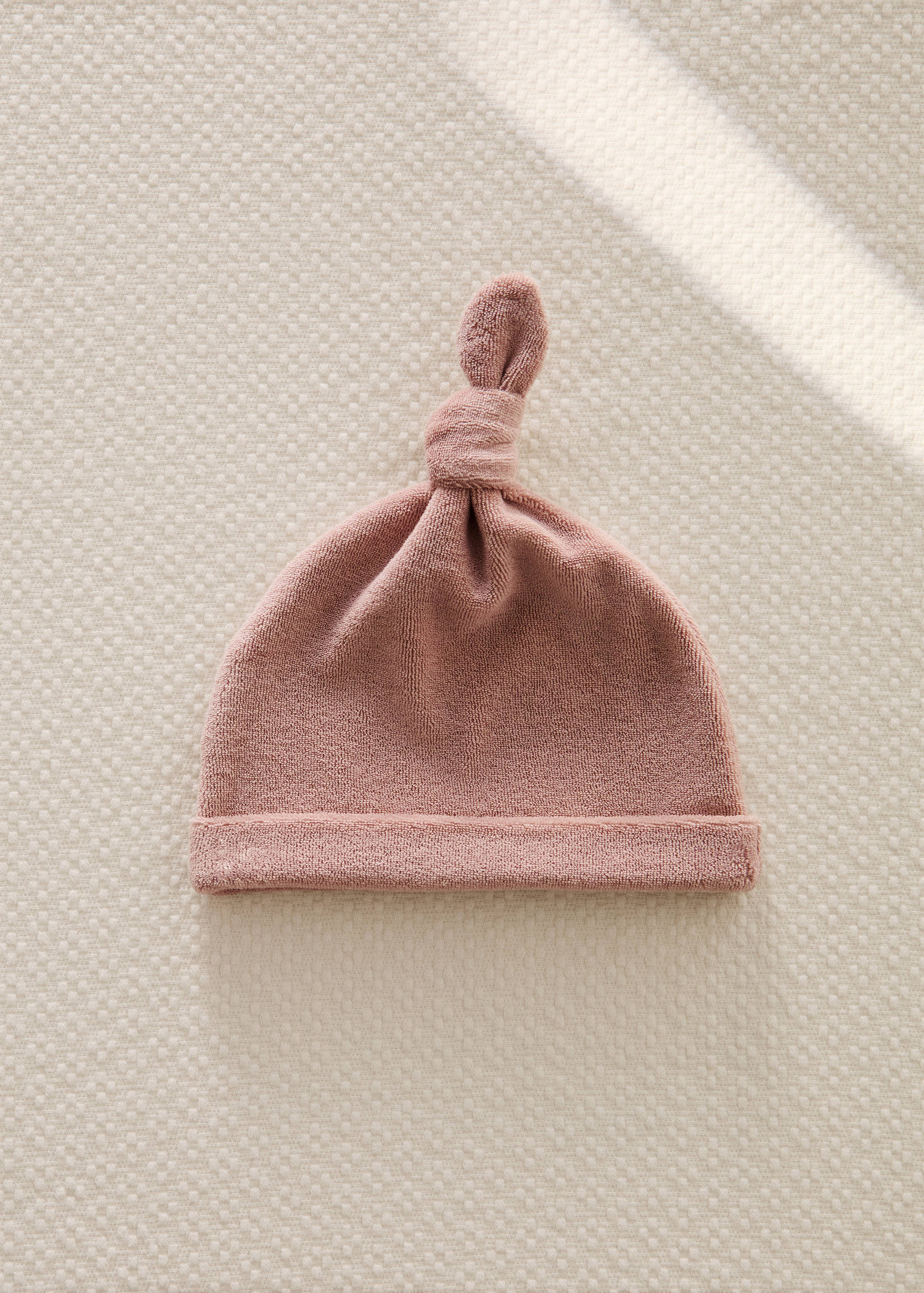 Dusty pink terrycloth baby hat with a folded brim and top knot.