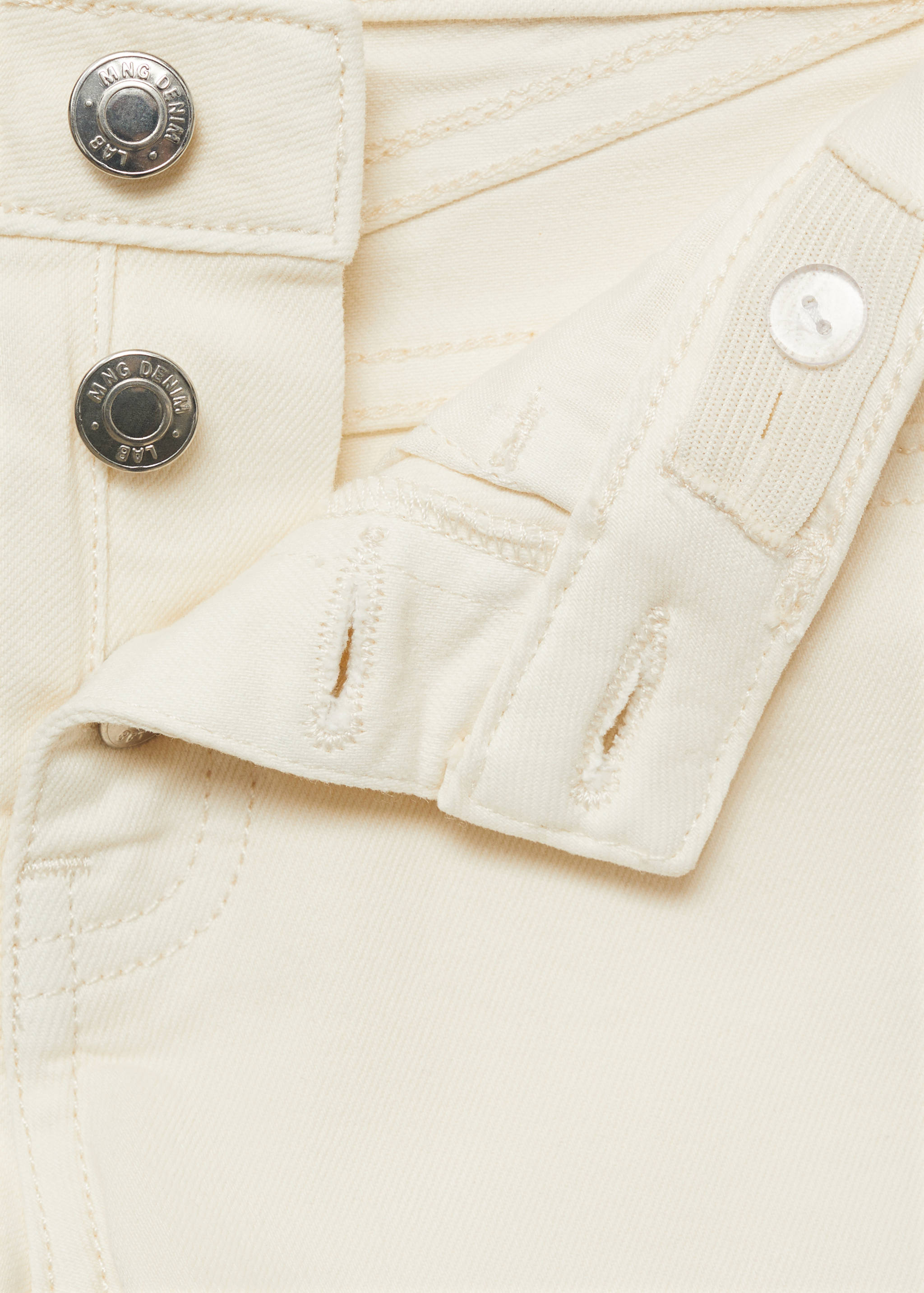 Cream denim shorts close-up showing metal buttons and waistband.