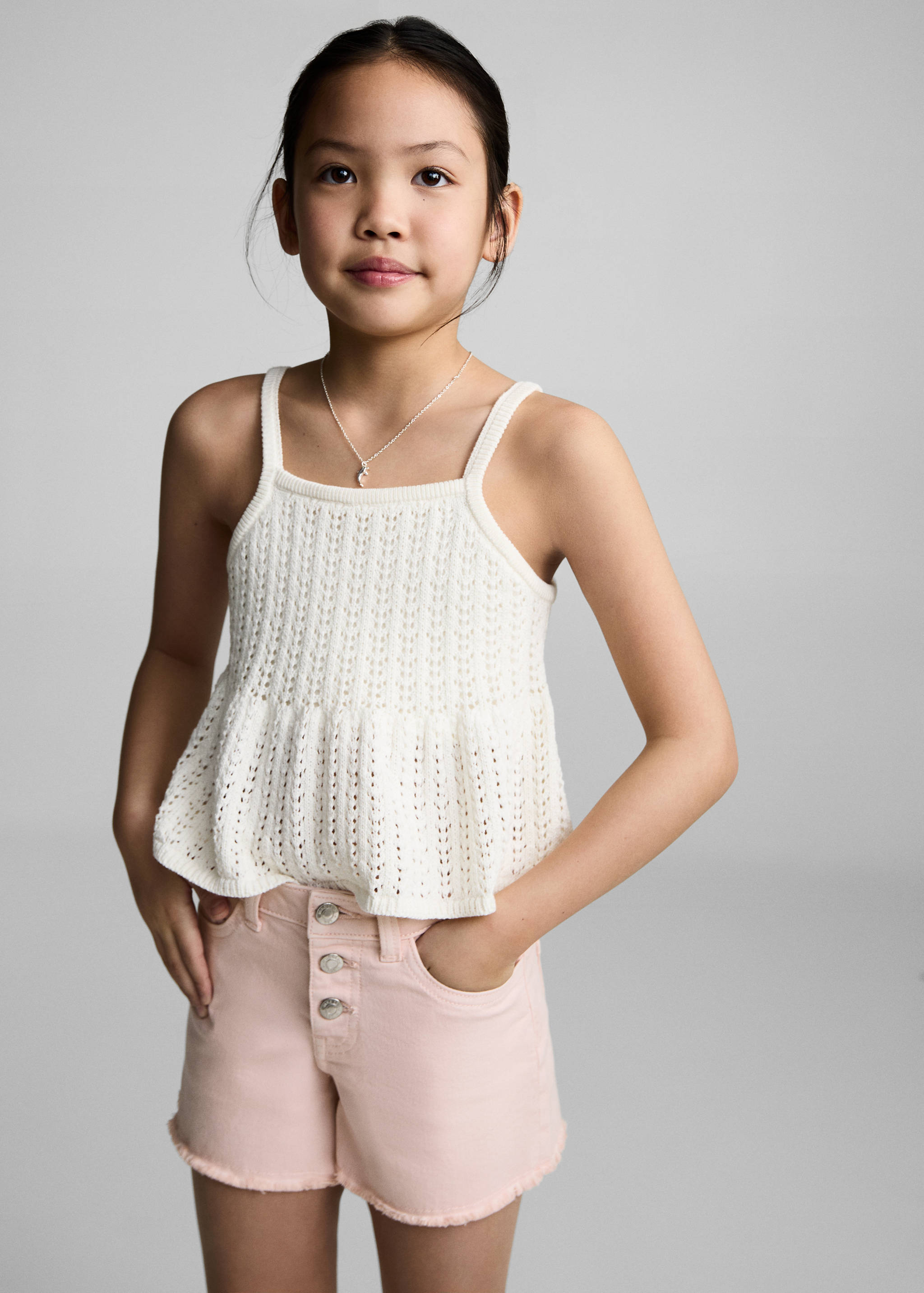 Pink denim shorts with a button fly and raw hems, styled with a white knitted top.