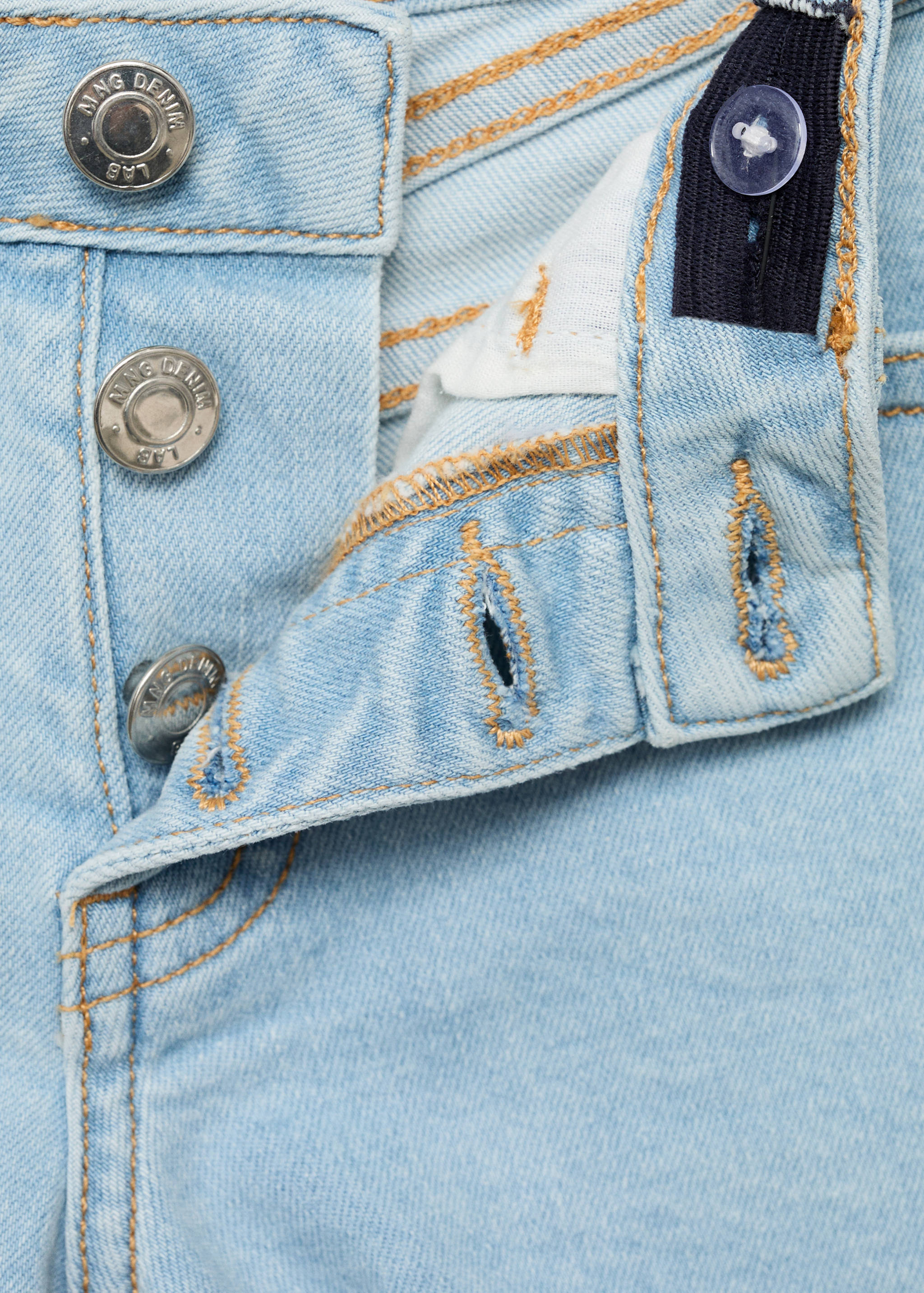 Close-up of the button fly and waistband of light wash denim shorts.