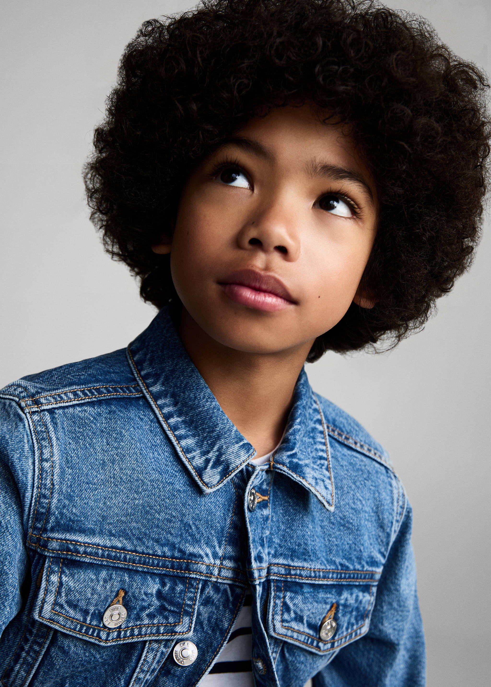 Close-up of a blue denim jacket with contrast stitching and chest pockets worn by a child.