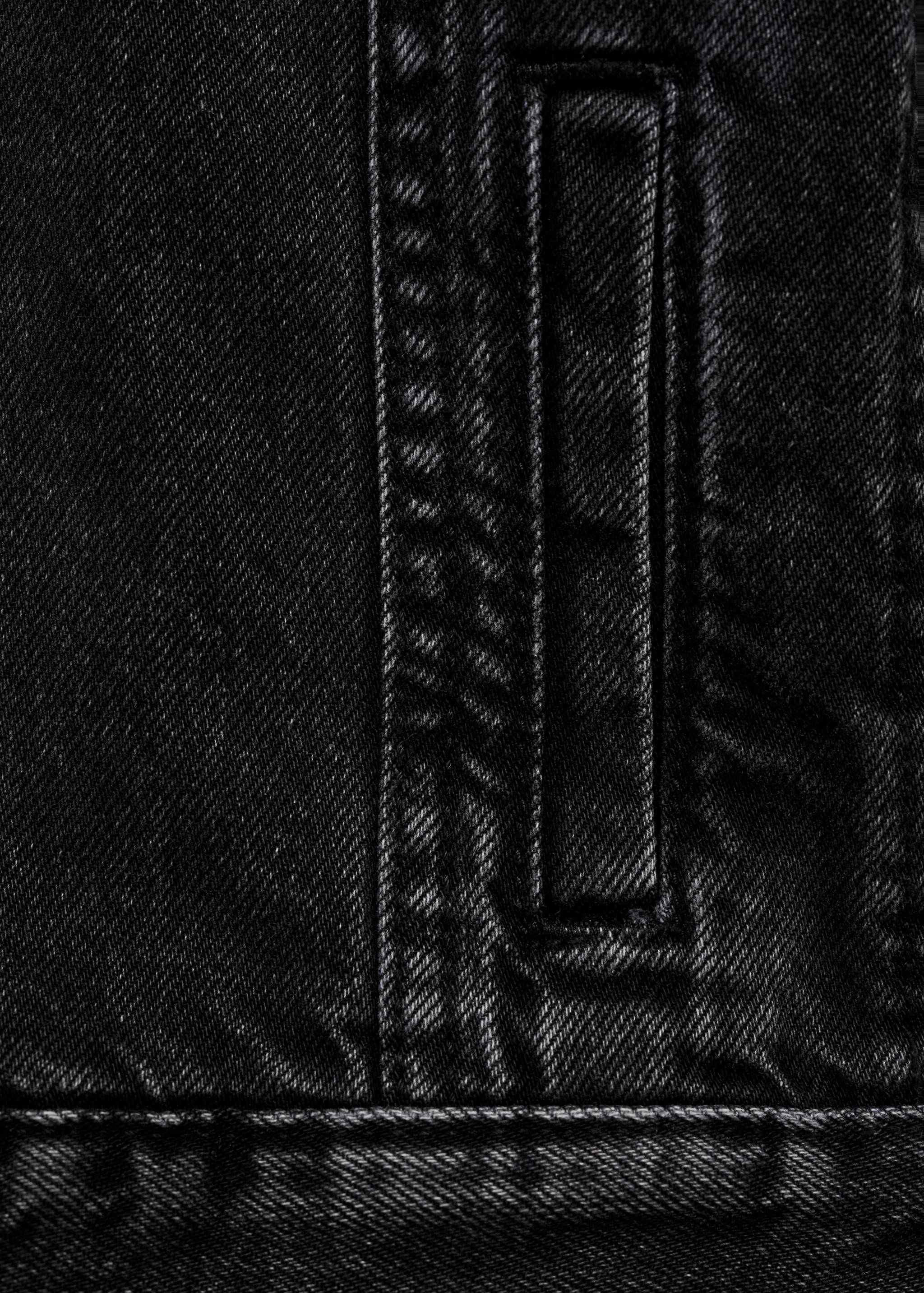 Close-up of black denim jacket fabric featuring a pocket and topstitching.