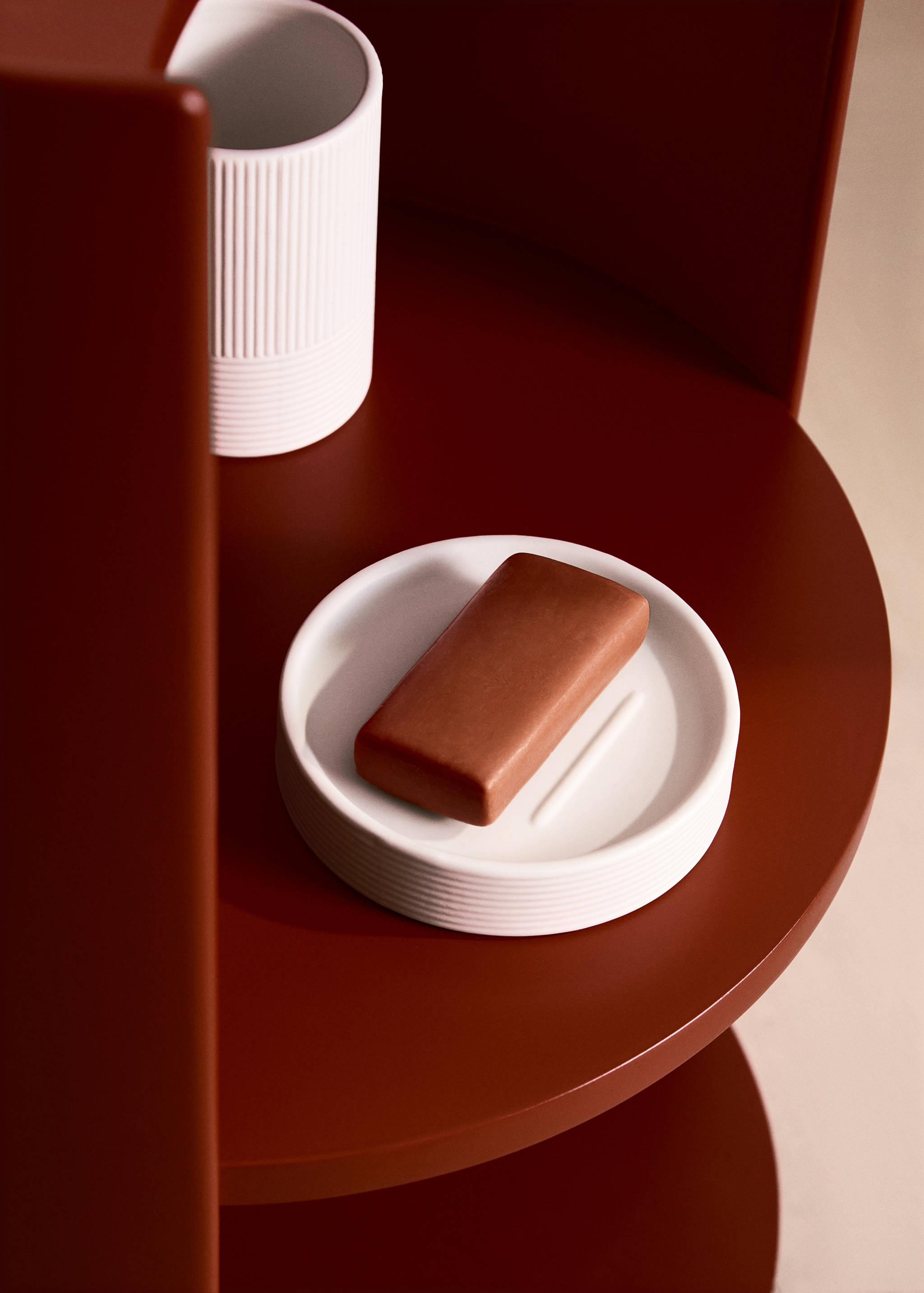 White ribbed soap dish holding a brown bar of soap on a dark red shelf.