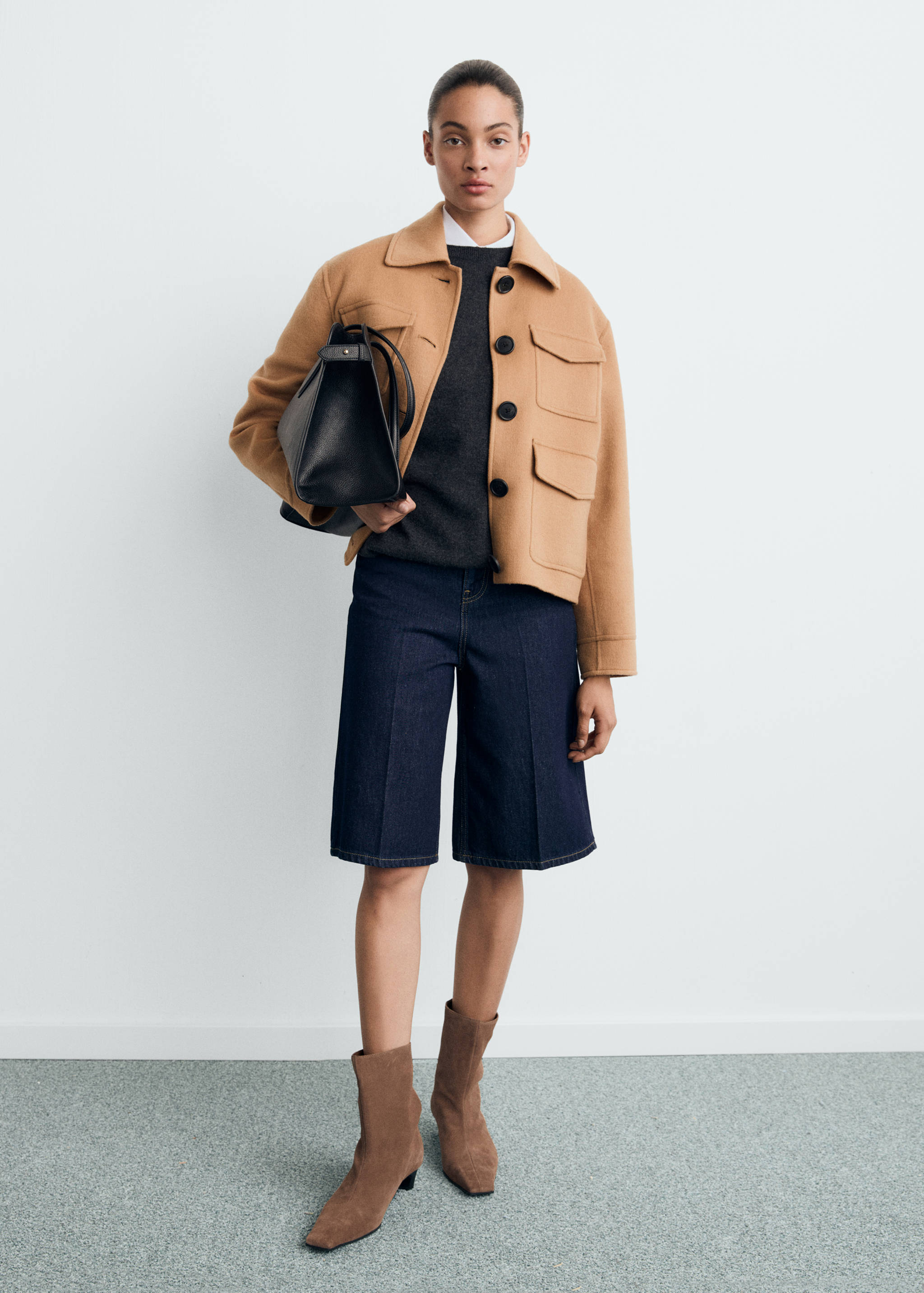 Camel jacket with flap pockets and large black buttons, styled with a grey sweater and denim shorts.