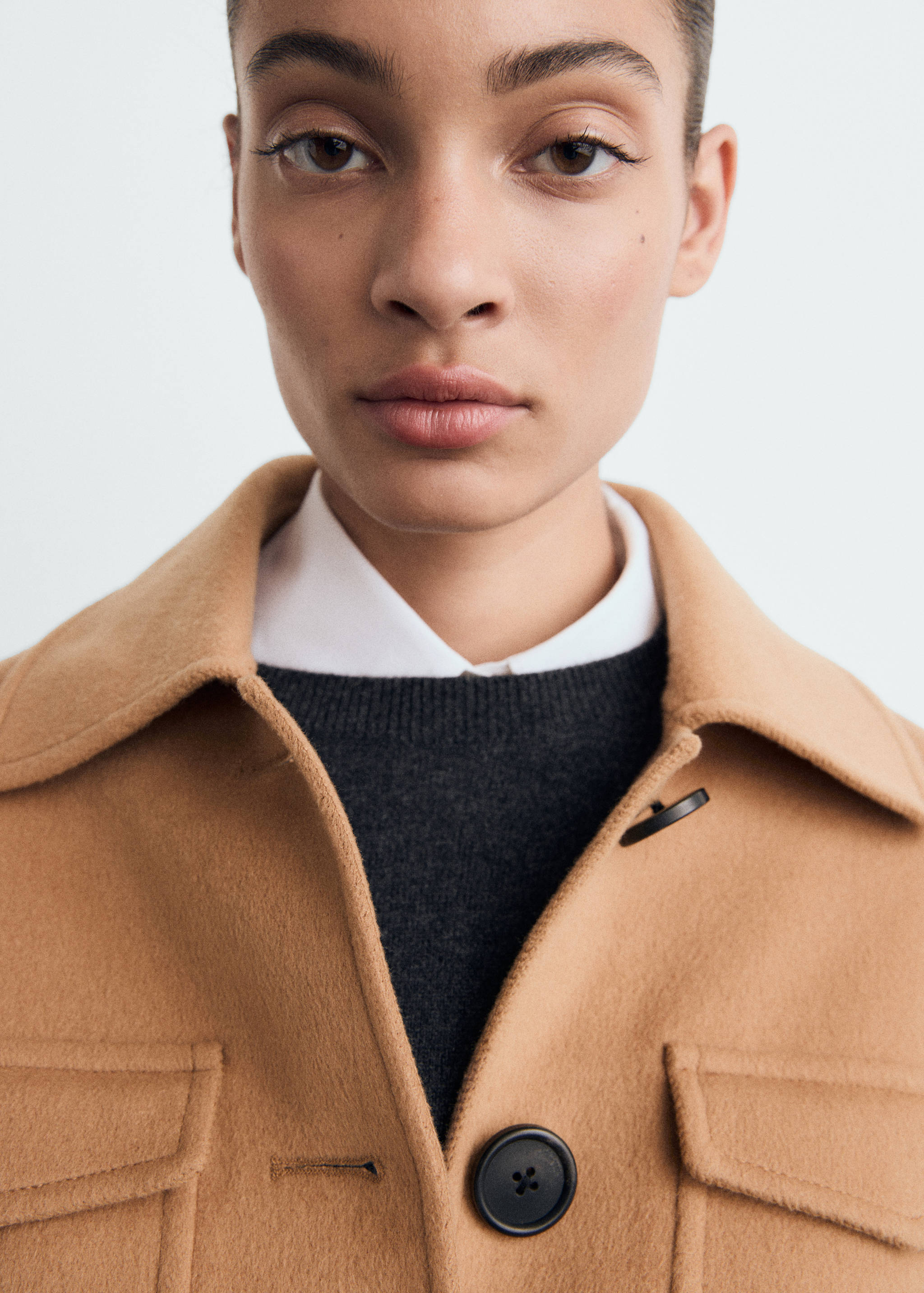 Close-up of a camel jacket with flap pockets and dark buttons.