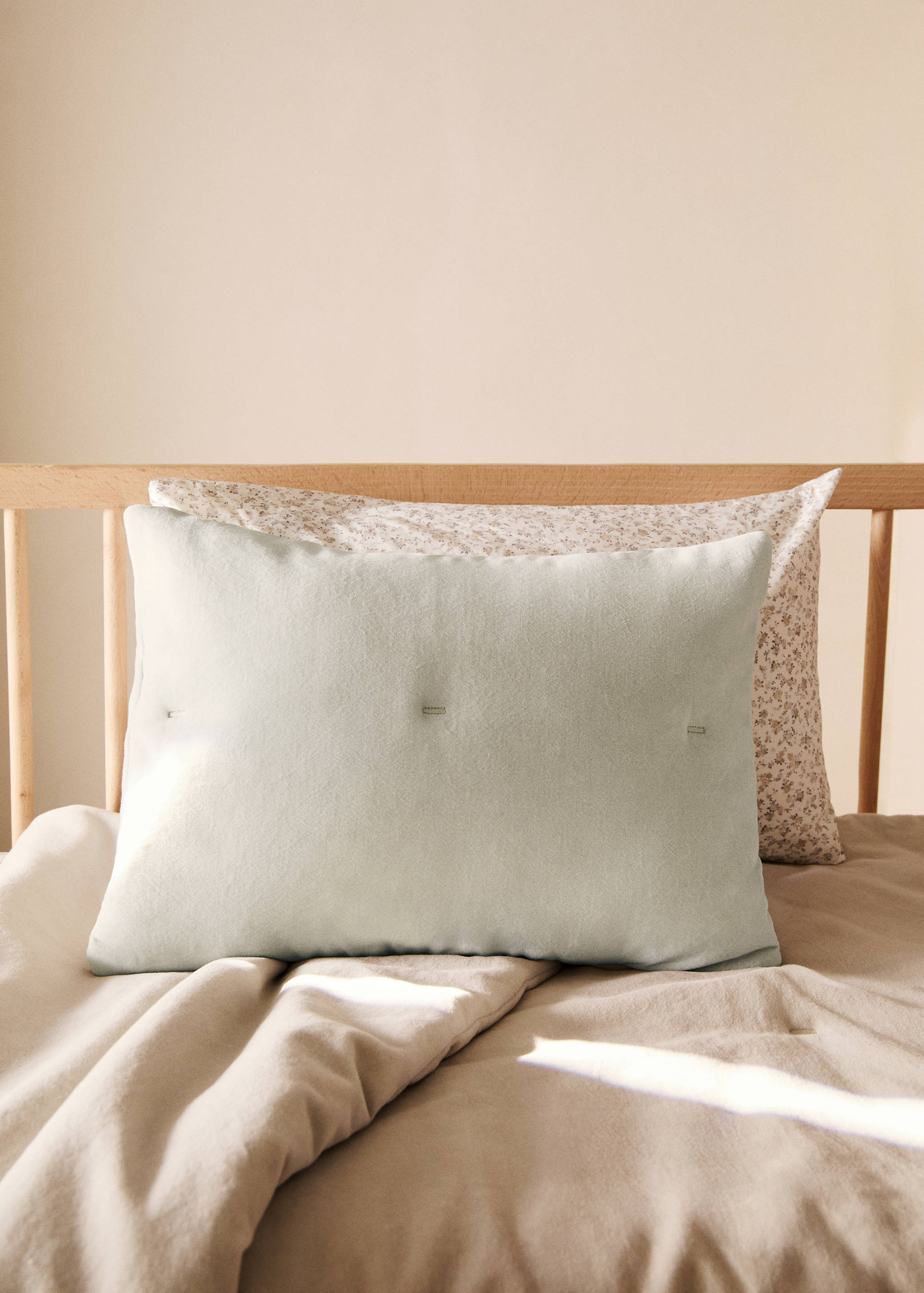 Light green rectangular cushion cover with stitched tack details on a bed.