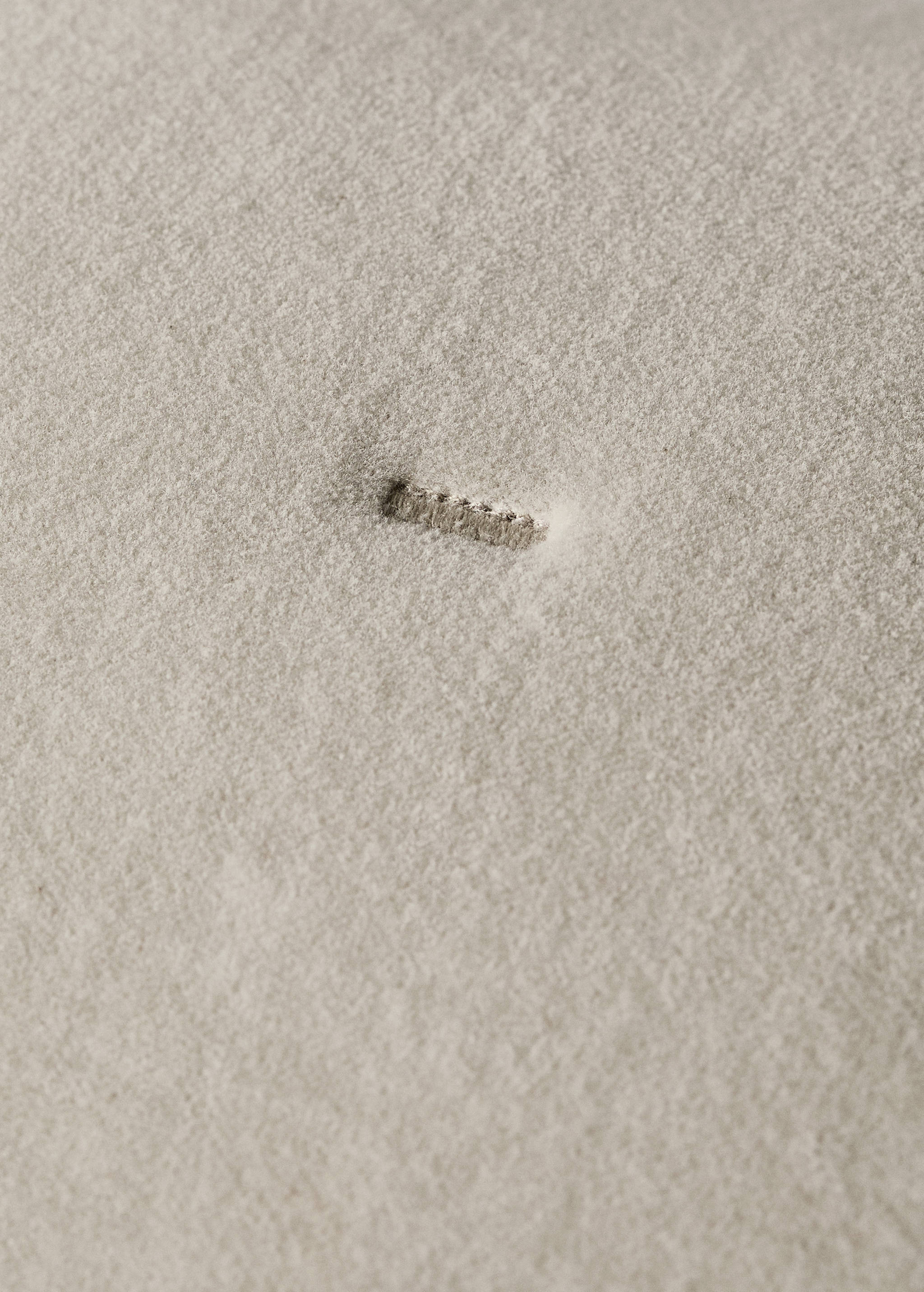 Close-up of a beige cushion cover showing fabric texture and a buttonhole.