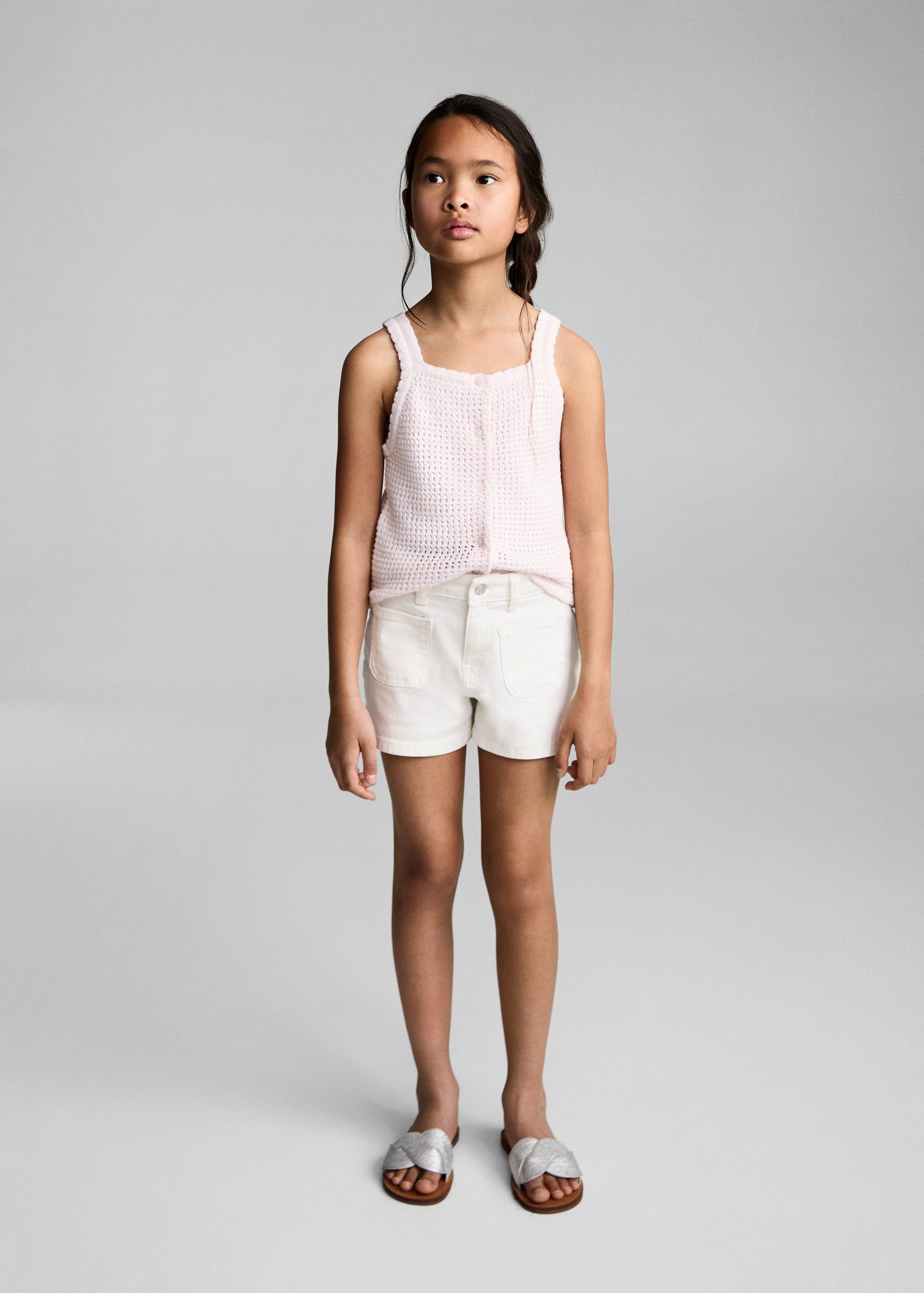 White denim shorts worn with a pink knit top and silver sandals.