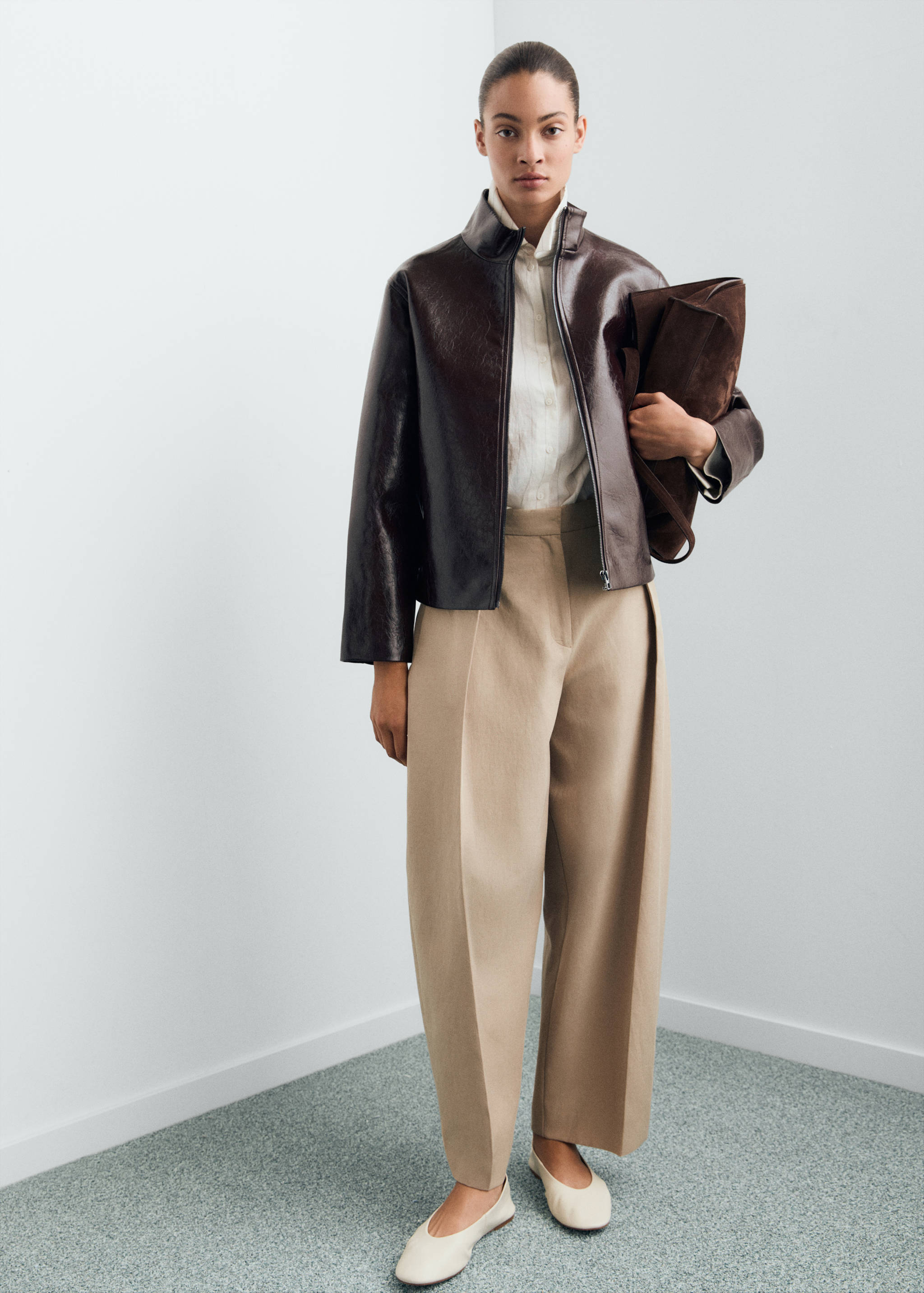 Dark brown glossy jacket with a structured collar, worn with a white shirt and beige trousers.