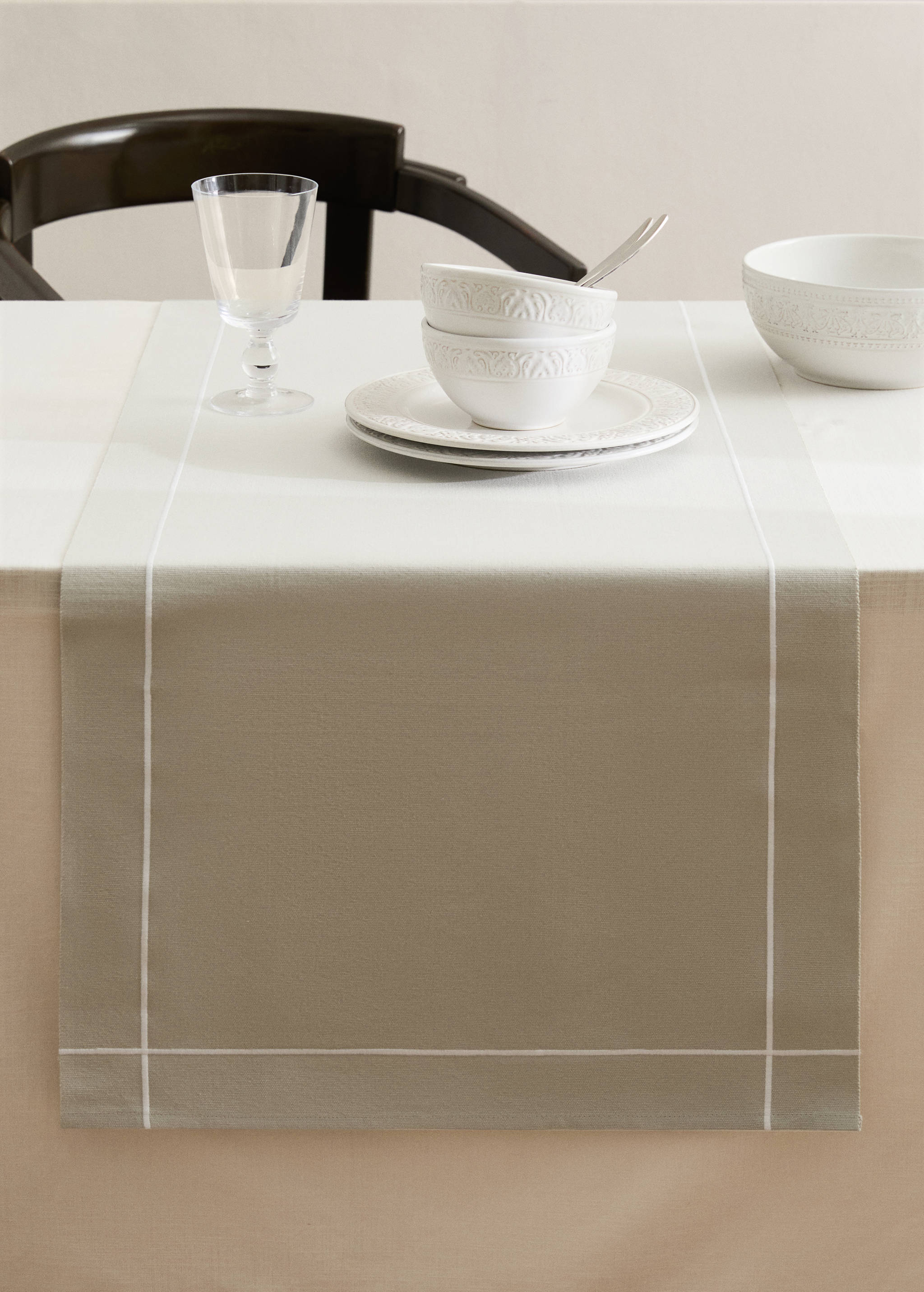 Beige table runner with white border stripe on a laid dining table.