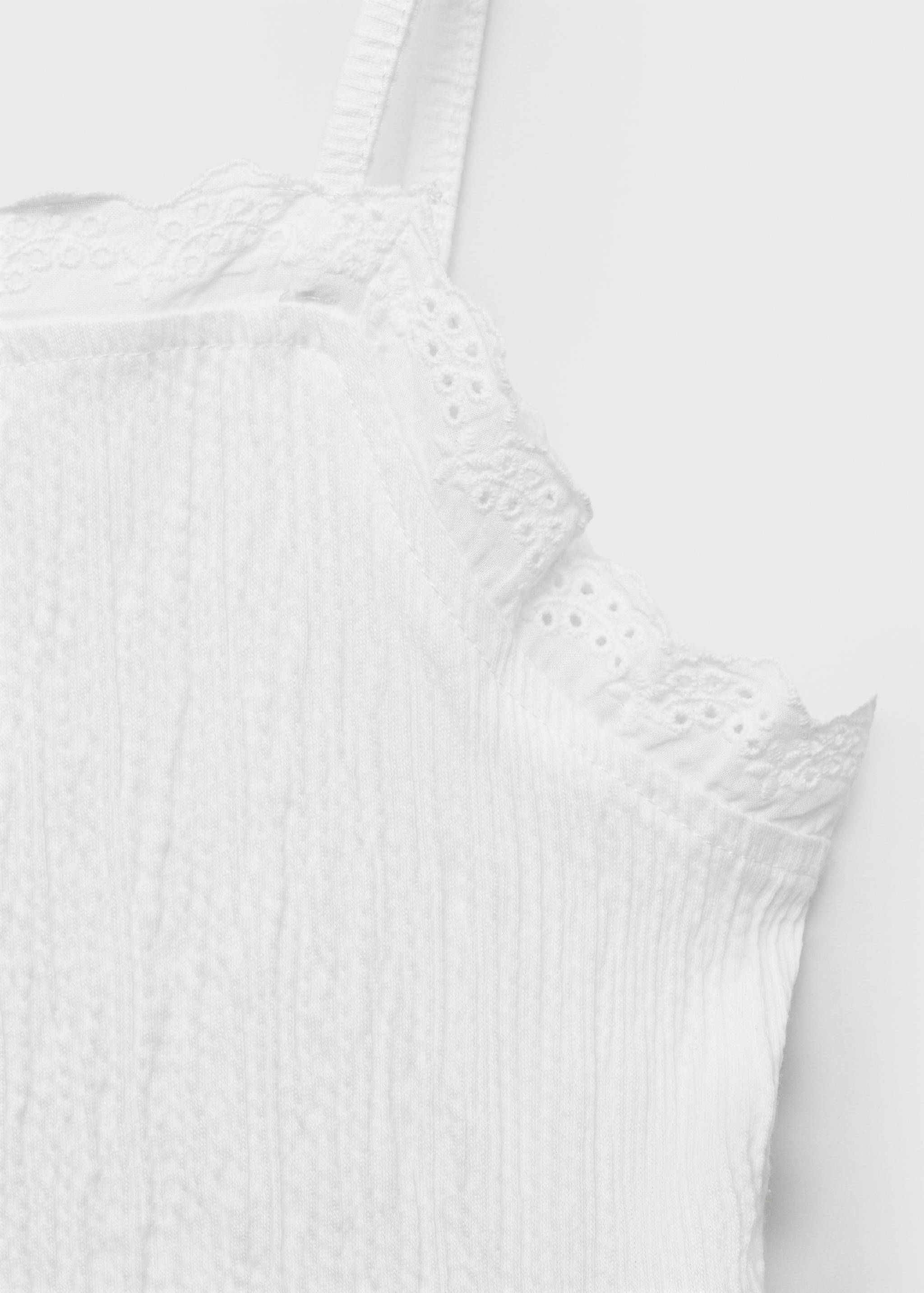 Close-up of a white kids' top with eyelet trim and straps.
