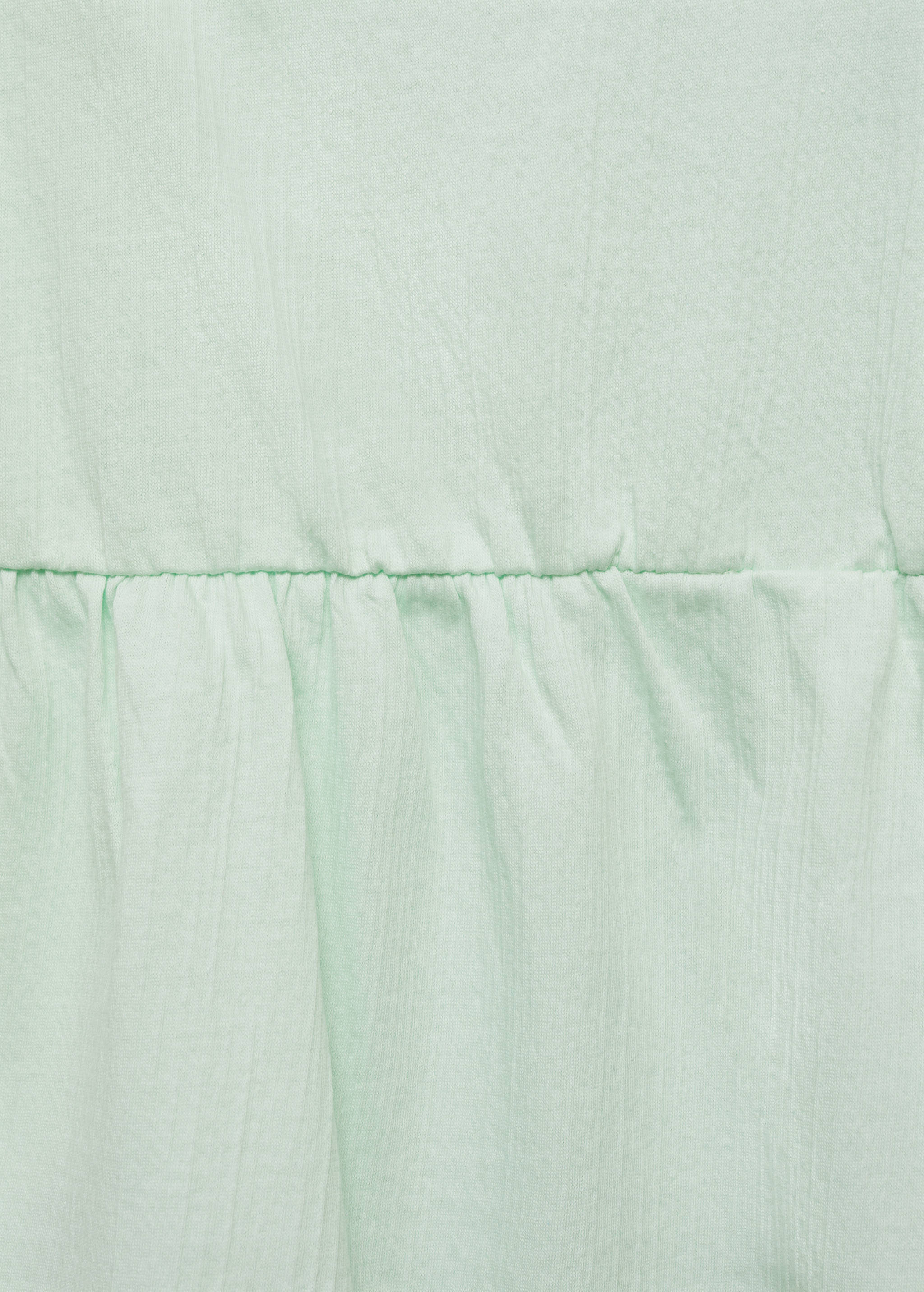 Close-up of light green top fabric with a gathered seam detail.