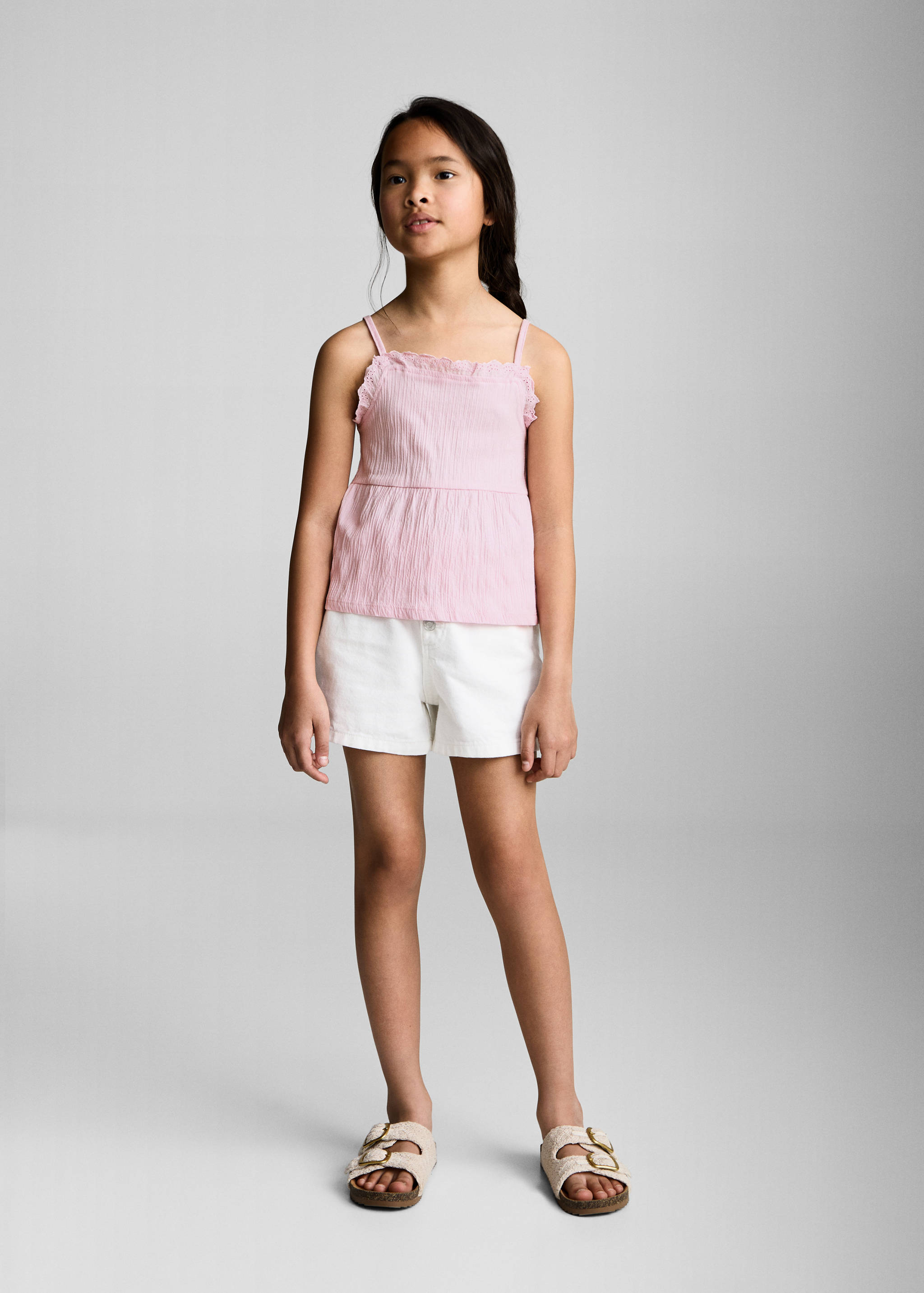 Pink sleeveless top with thin straps and a ruffled neckline, styled with white shorts.