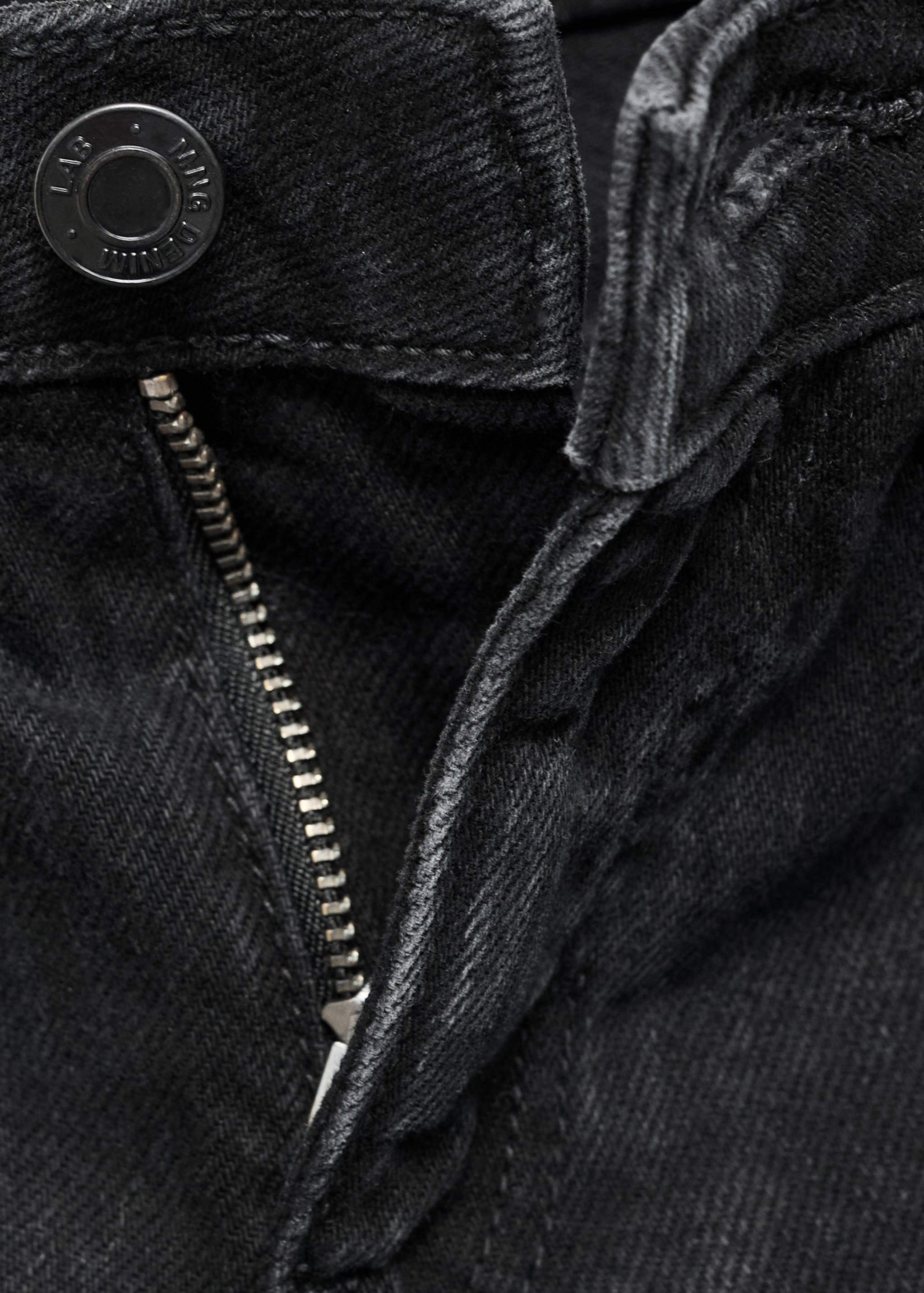 Close-up of black denim bermuda shorts button and zip fly.